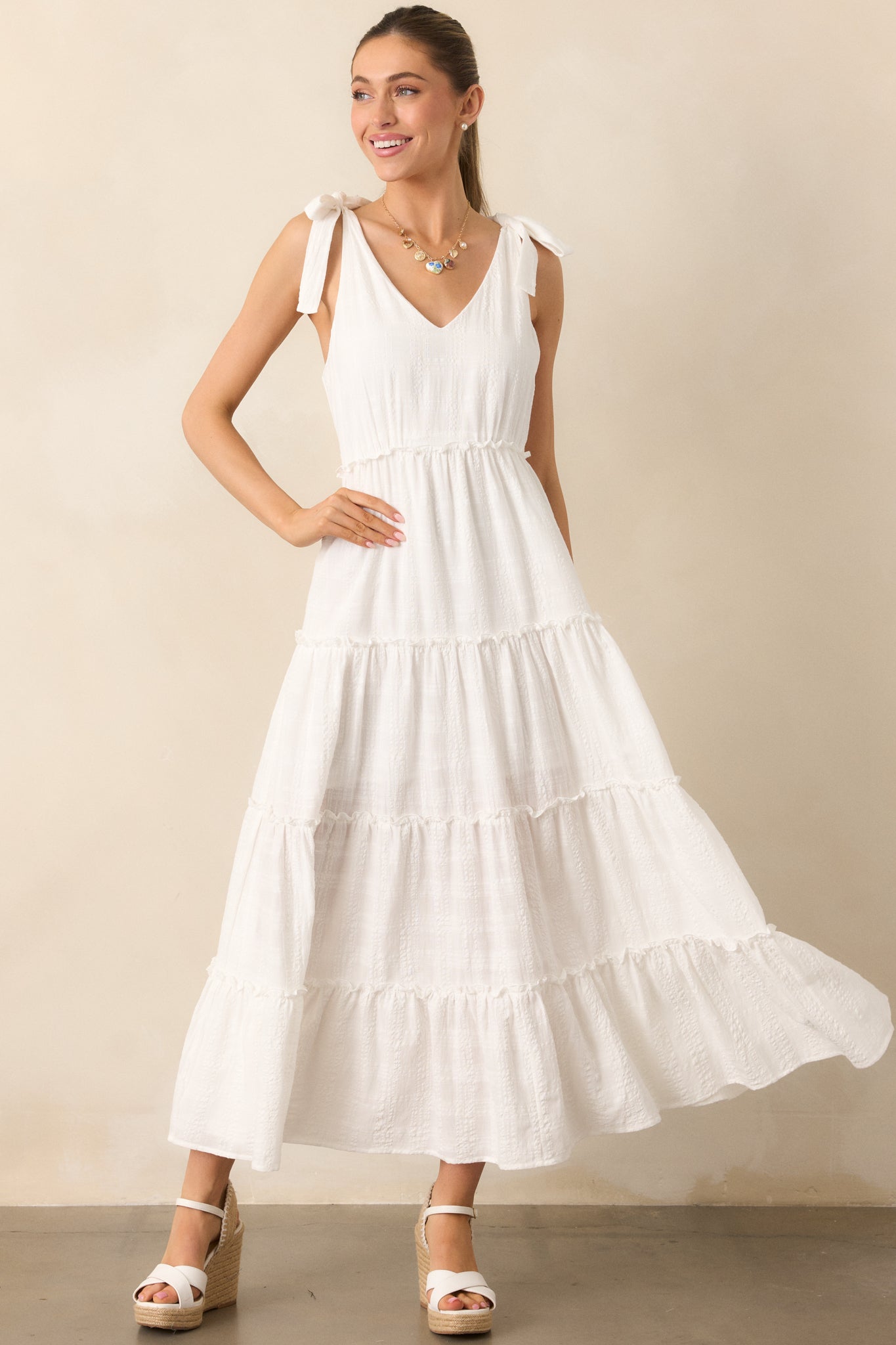 A lovely ivory dress with a soft v-neckline, lightweight textured fabric, and self-tie bow straps, complete with a tiered, ruffled skirt for a flowy, feminine look.