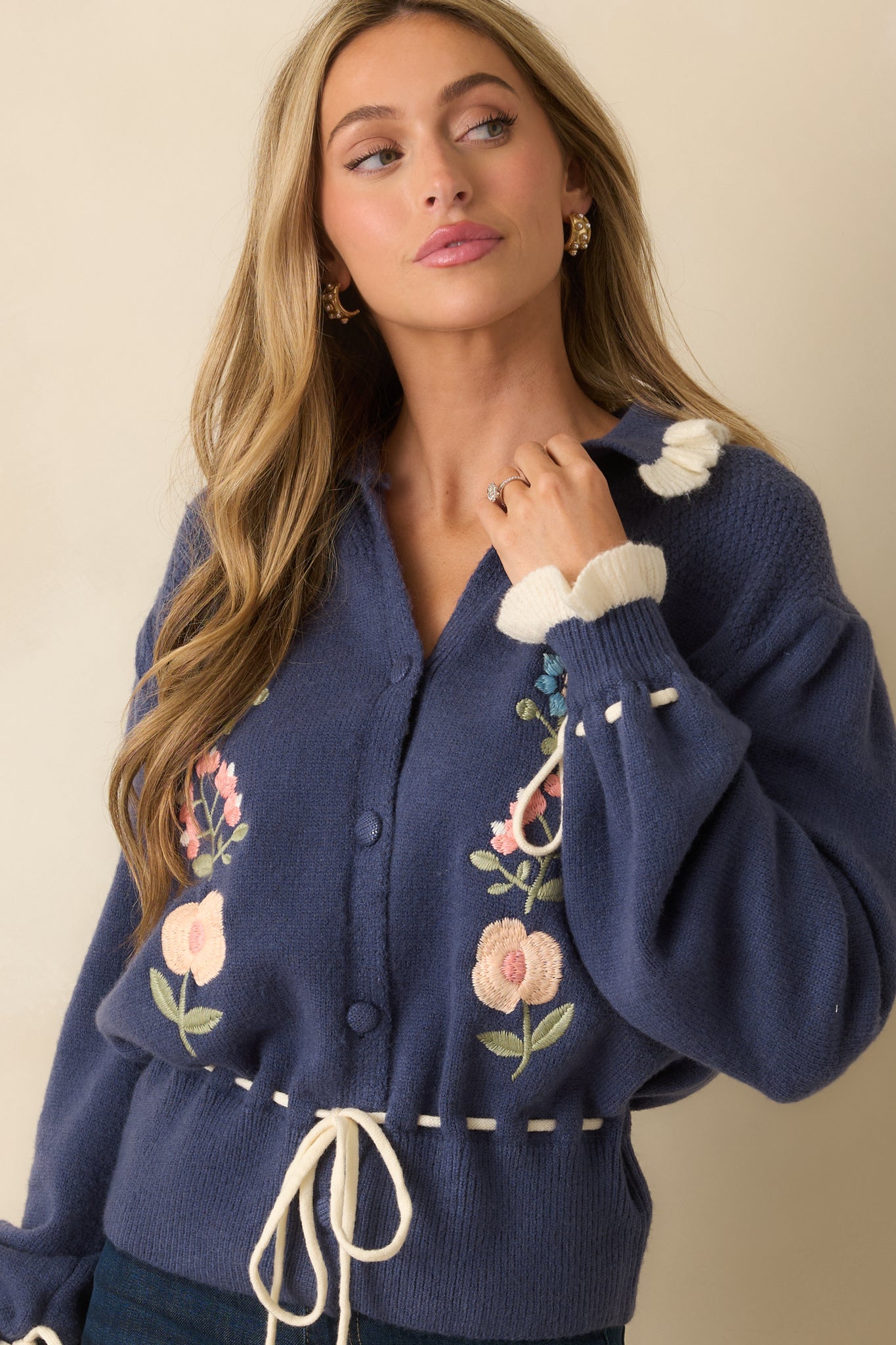 Close view of the floral embroidery and ivory ruffle trim along the collar of the dusty blue cardigan.