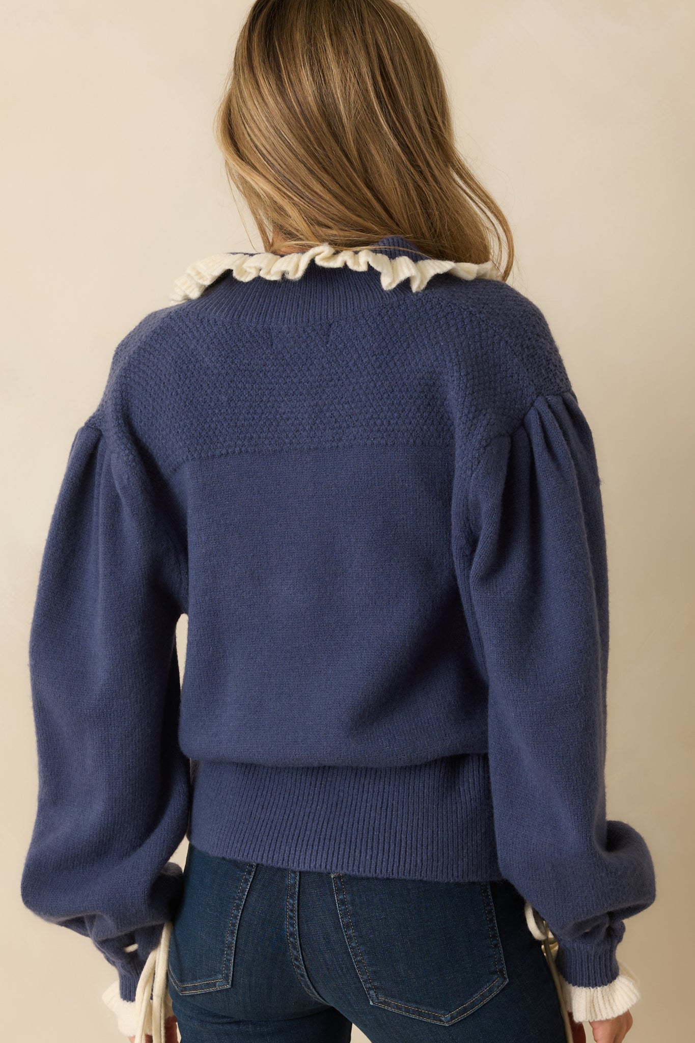 Rear view of the dusty blue cardigan highlighting the smooth knit back and long sleeves with tie ruffle trim.