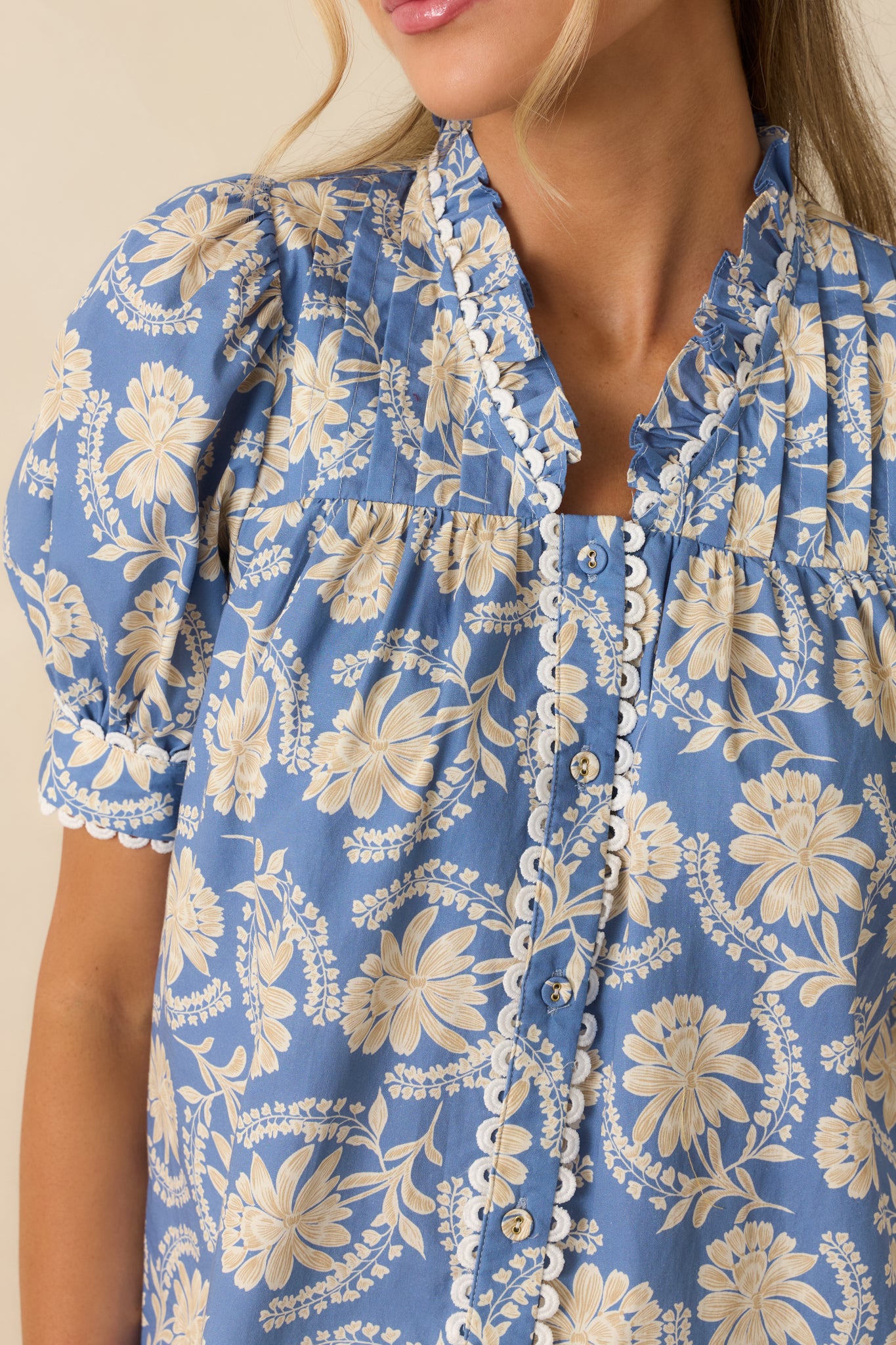 Close-up detail of the dusty blue and ivory floral blouse highlighting the ruffled collar, scalloped trim, and button accents
