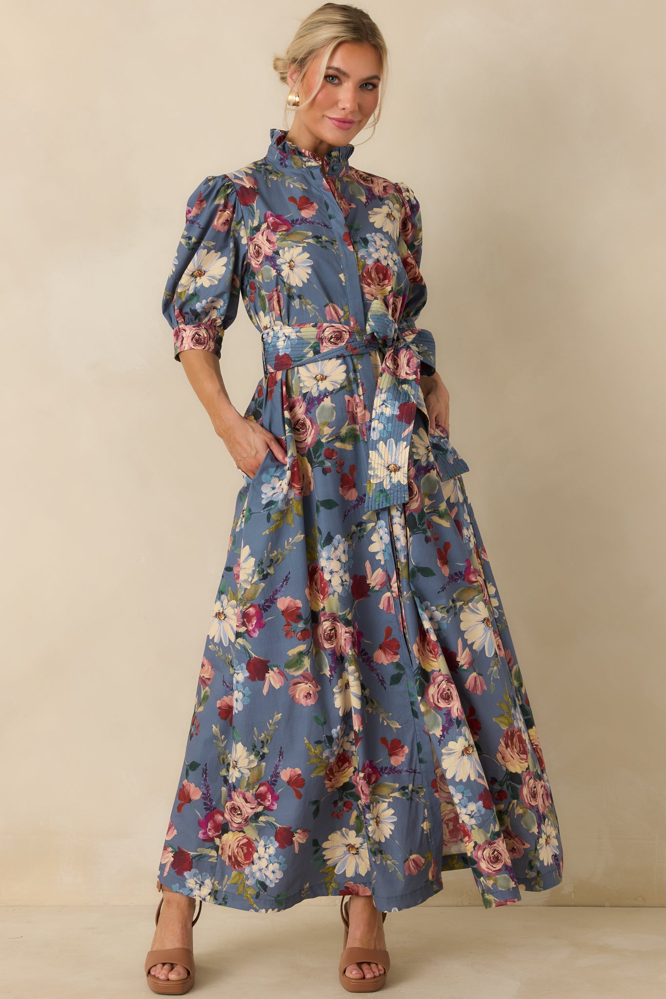 Dusty blue floral maxi dress showcasing blush, burgundy, ivory, and green garden blooms with a coordinating self-tie belt.