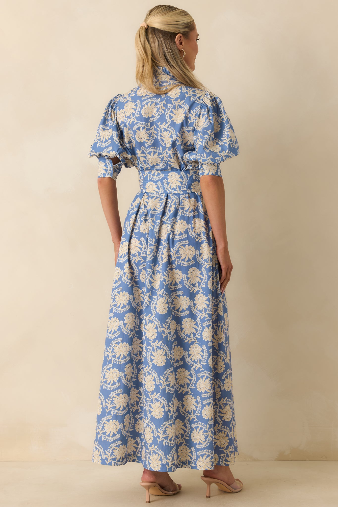 Rear view of the dusty blue and ivory floral maxi dress highlighting the self-tie waist, puff sleeves, and flowing full-length skirt.