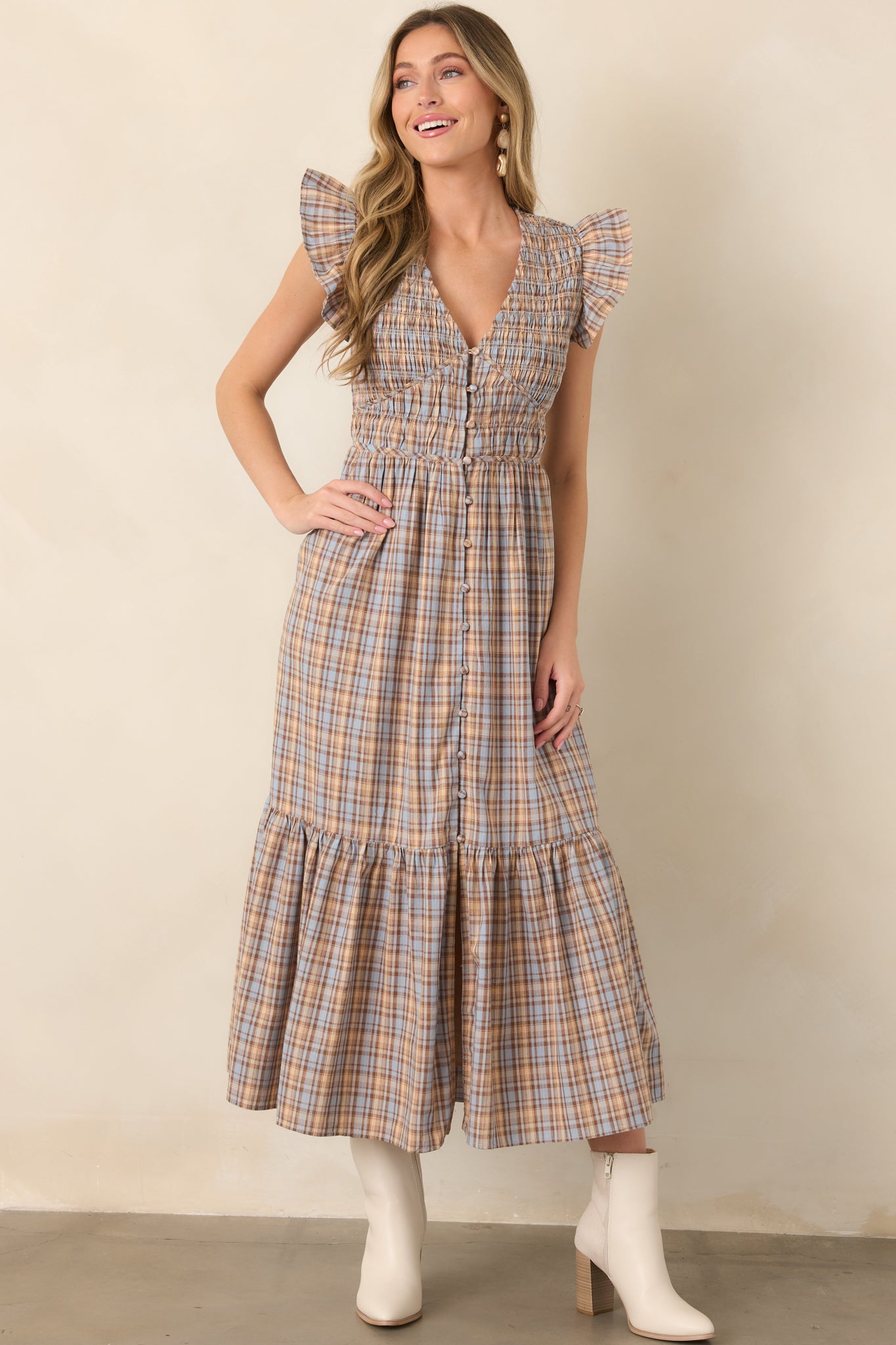 Dusty blue, tan, and brown plaid midi dress featuring a deep V-neckline, smocked bodice, flutter sleeves, and covered front buttons.