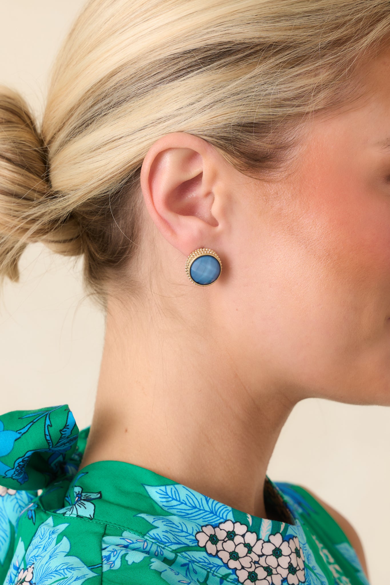 Gold stud earrings featuring a faceted blue stone center framed by a delicate gold halo.