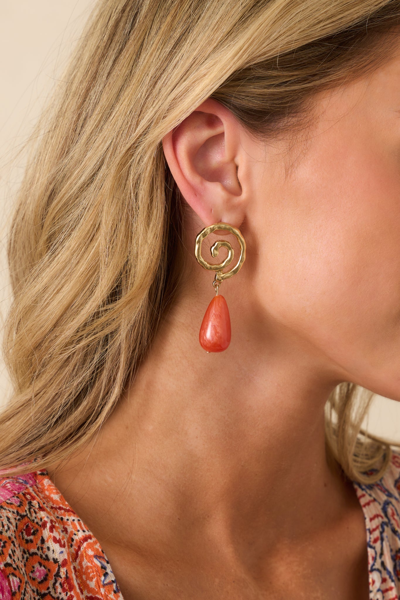 Cropped front view of the earrings showing the hammered gold swirl-shaped stud paired with a terracotta pearlescent drop charm.