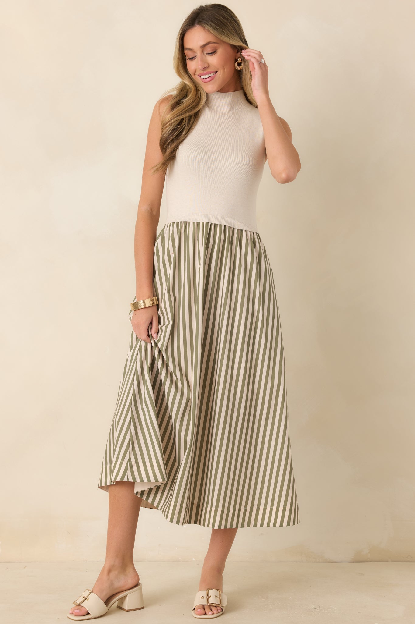 Ecru knit midi dress featuring a sleeveless mock neckline, fitted bodice, and a flowing sage green striped skirt with elegant movement.