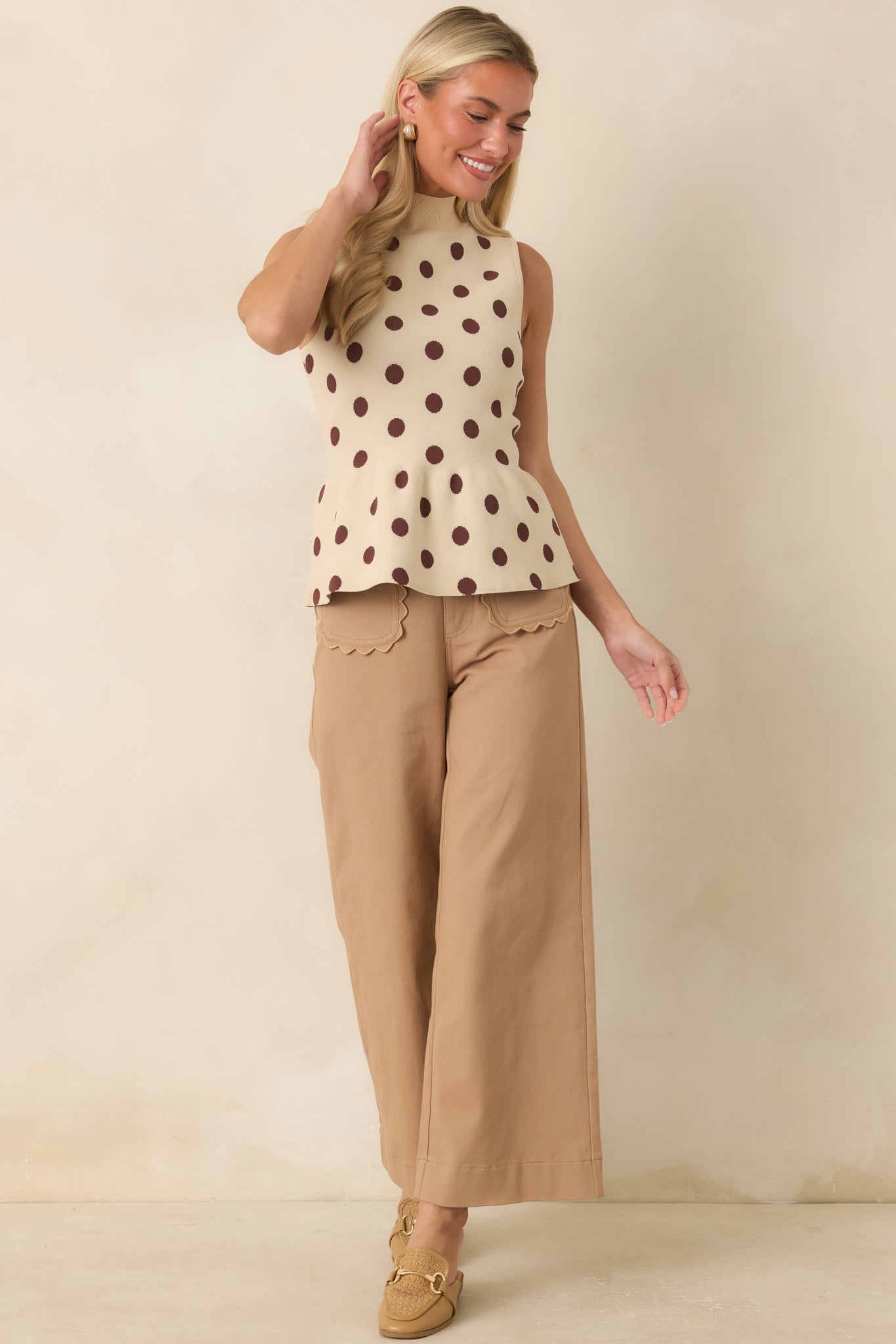 Ecru sweater knit top featuring a ribbed mock neckline, brown polka dot print, sleeveless silhouette, and subtle peplum hem.