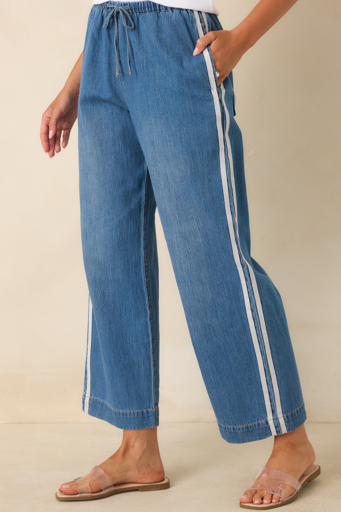 Detailed view of the elastic waistband with an adjustable drawstring on medium wash cotton denim pants accented by contrast side stripes.