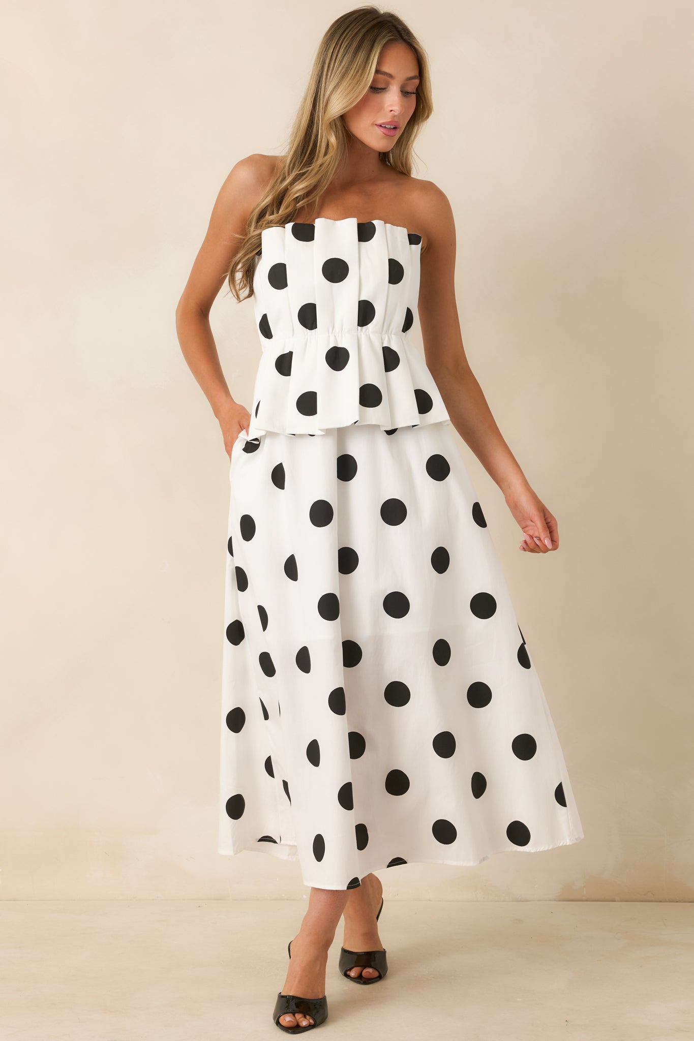 Elegant strapless midi dress designed with oversized black polka dots, a modern pleated peplum detail, and a full A-line skirt for easy movement.