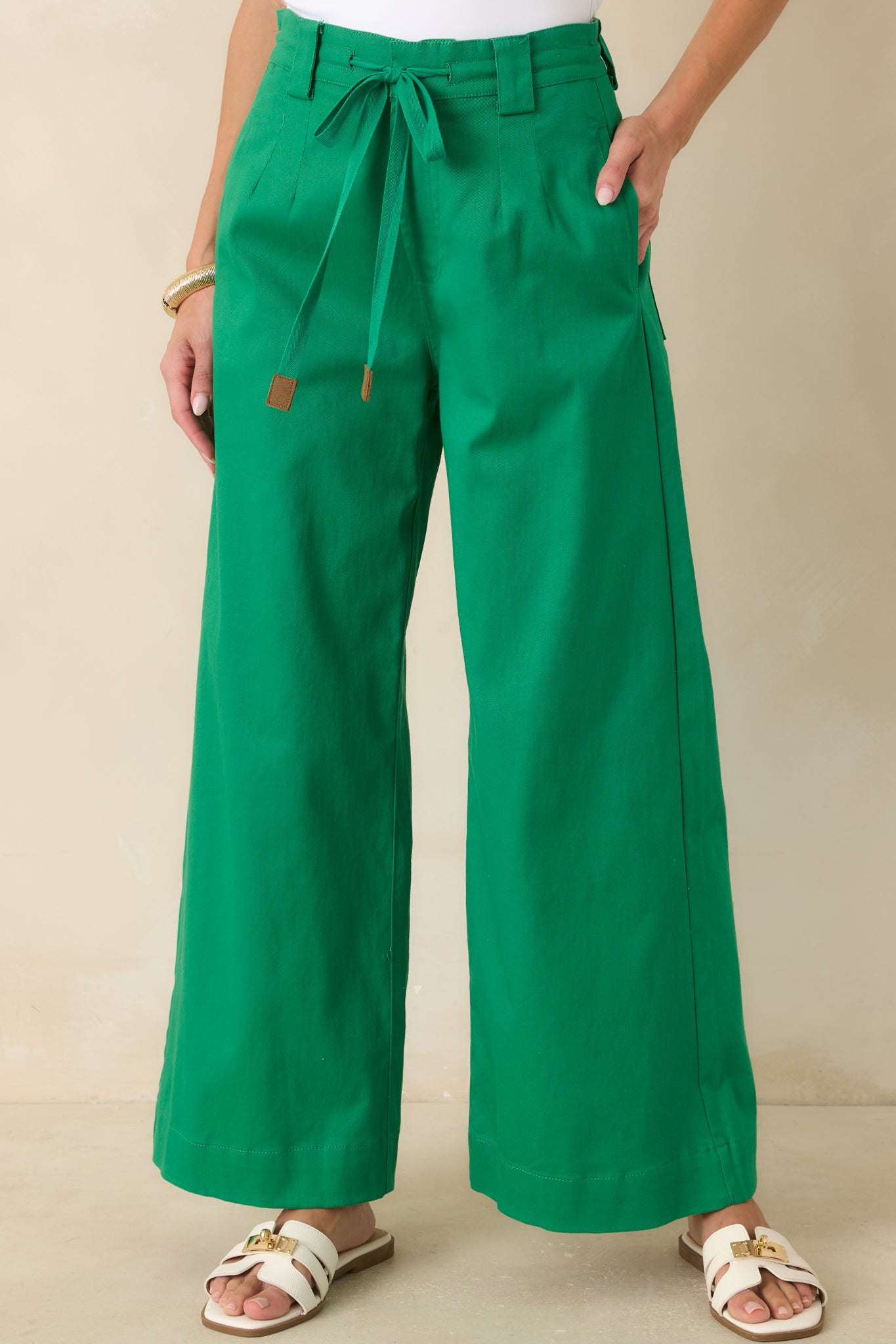 Close view of the emerald pants highlighting the tie belt, structured waistband, and front pleat details.