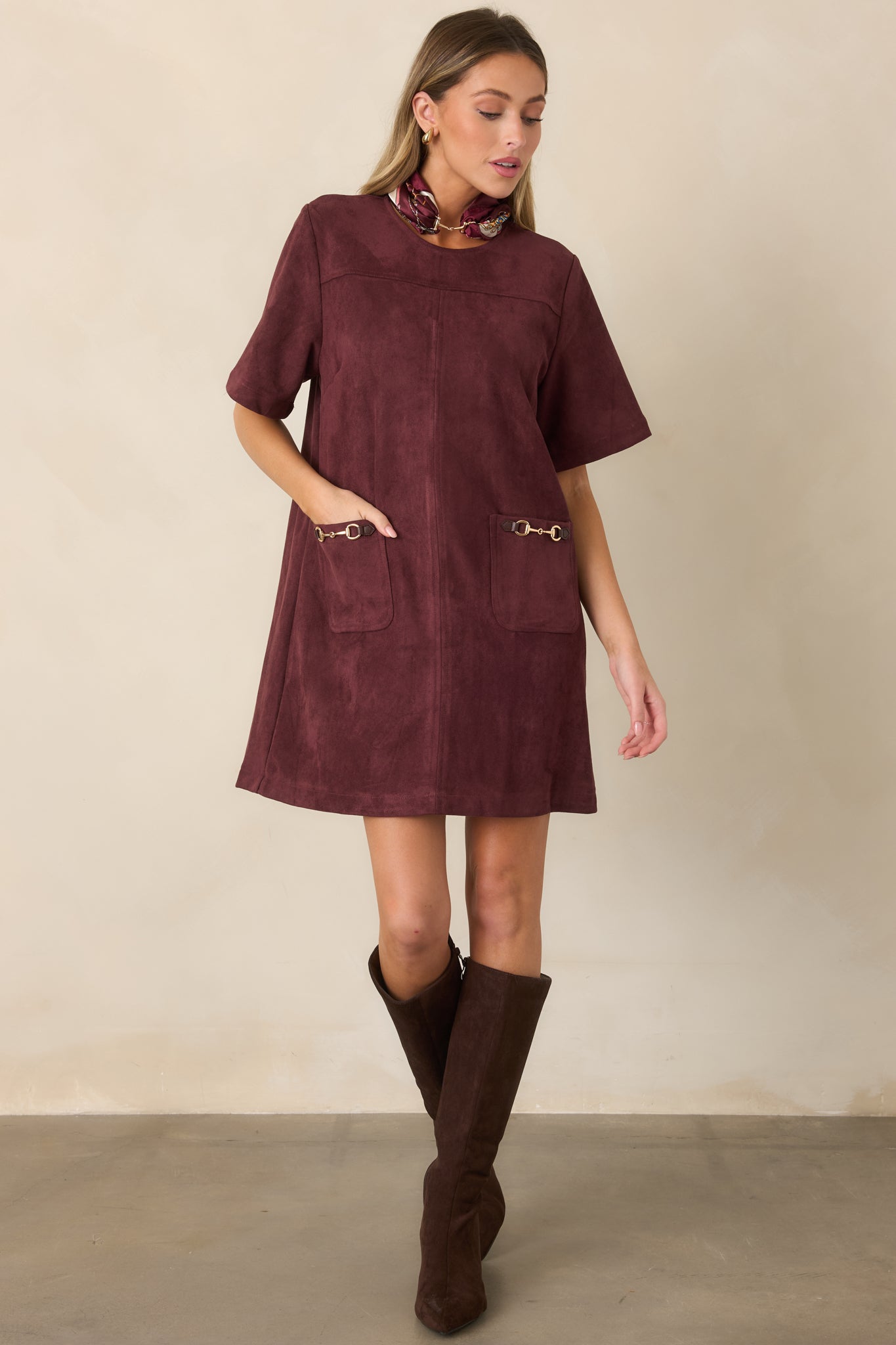Equestrian-inspired mini dress highlighting the clean round neckline, fitted short sleeves, front patch pockets, and polished metallic accents.