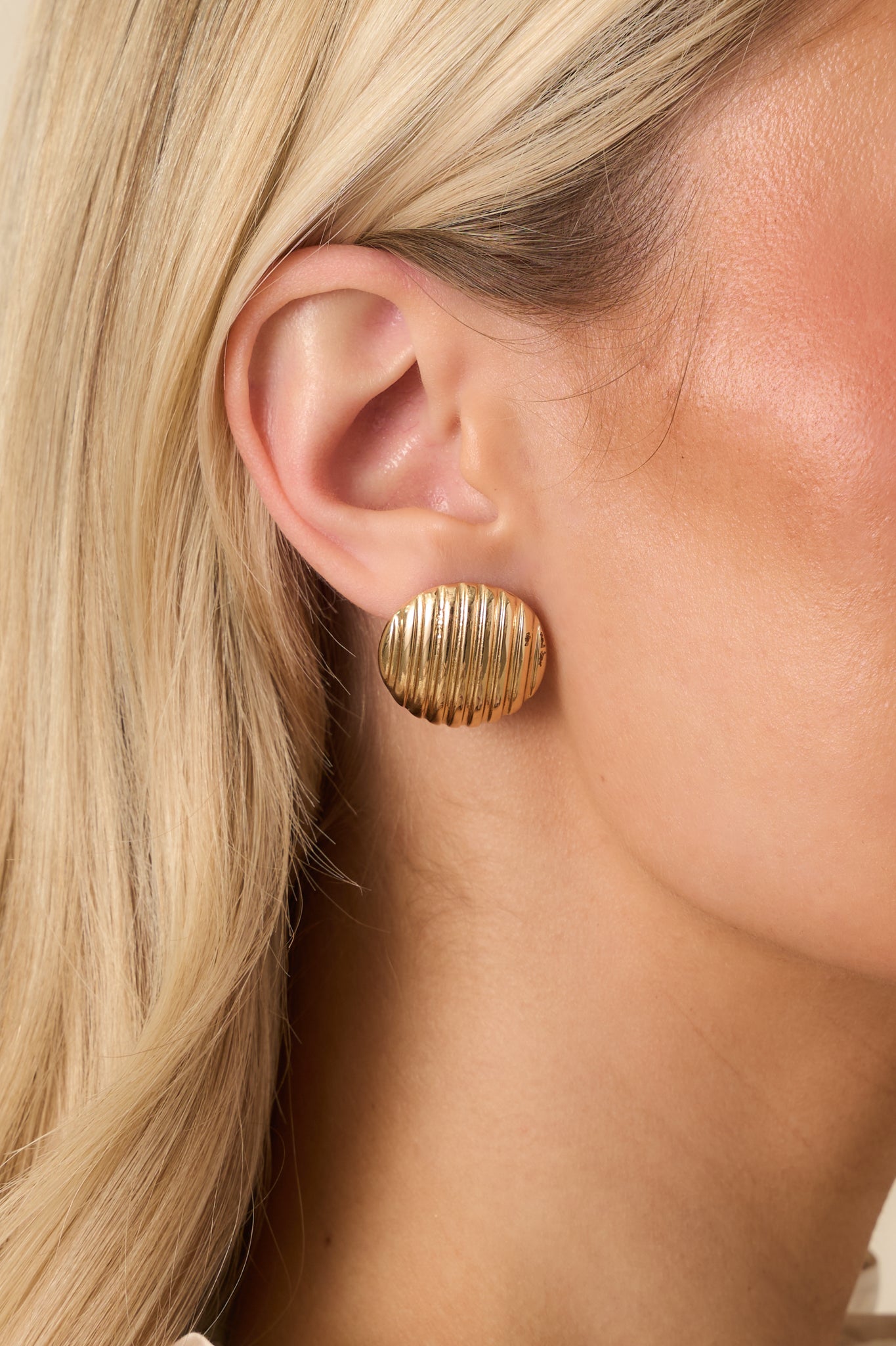 Extreme close-up of gold earrings highlighting ribbed design and polished finish.