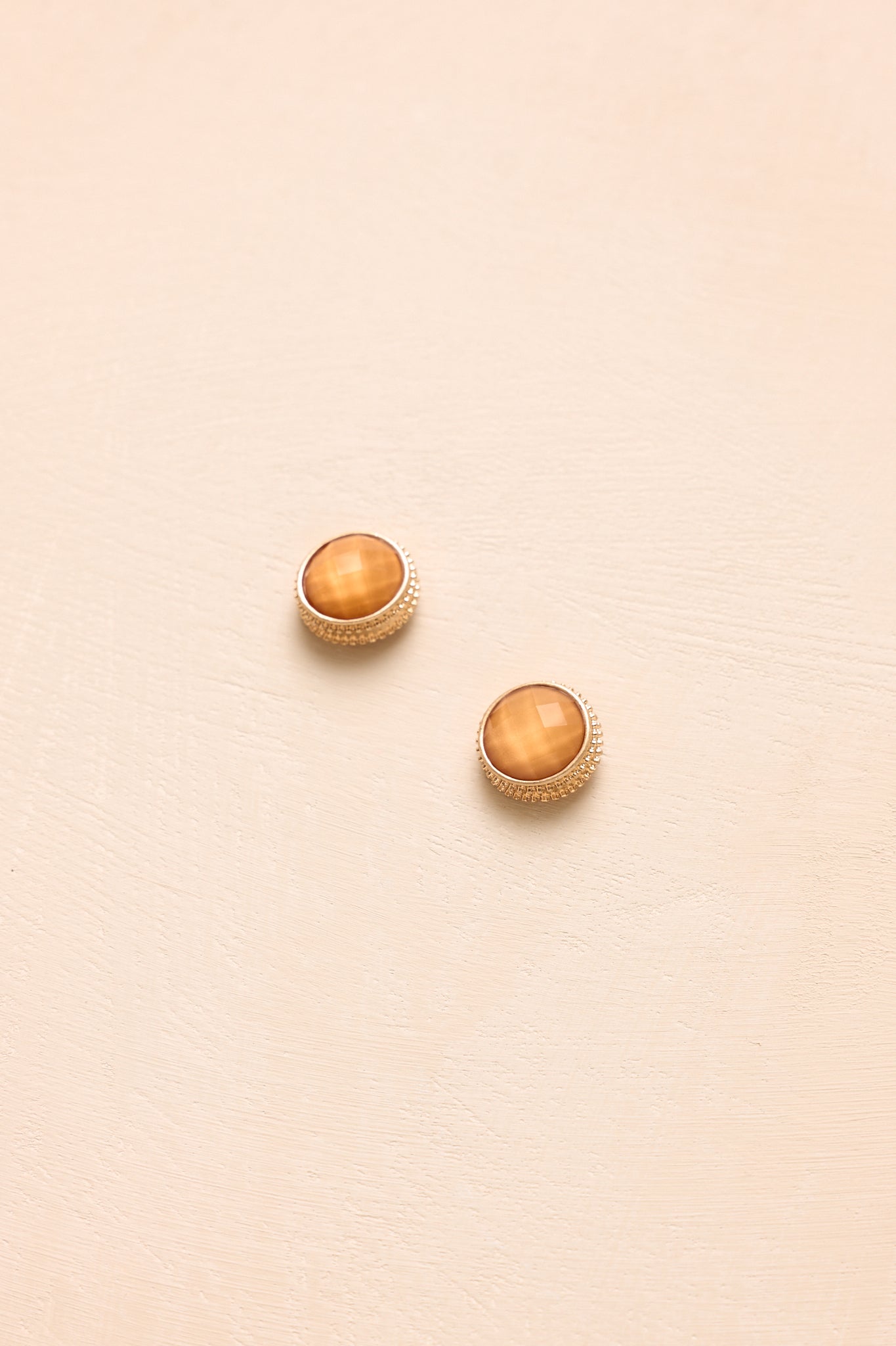 Faceted orange gemstone earrings with a polished gold-tone frame presented on a neutral beige backdrop.