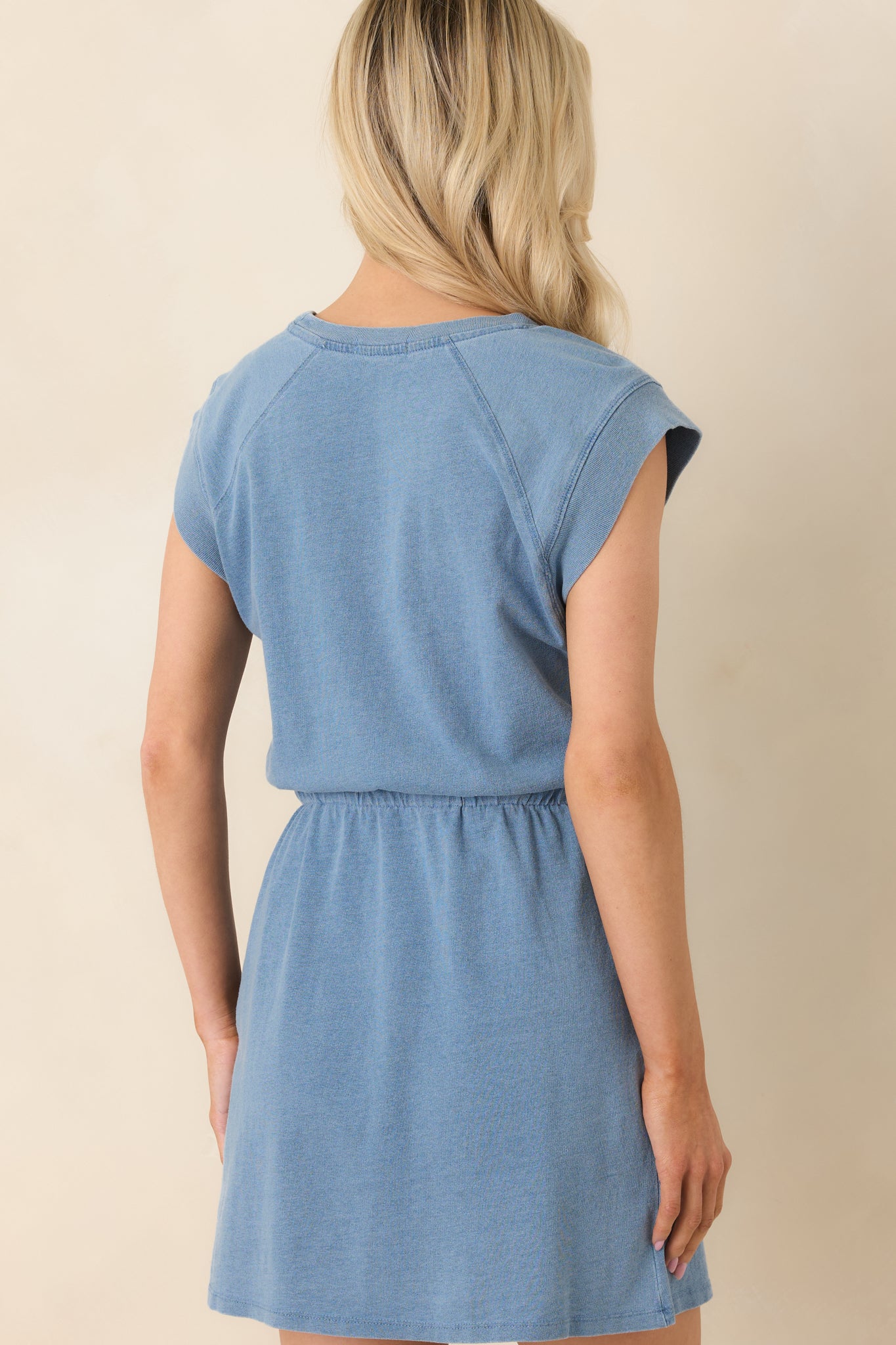 Back view of the faded indigo mini dress showing the relaxed silhouette, cap sleeves, and smooth cotton jersey fabric.