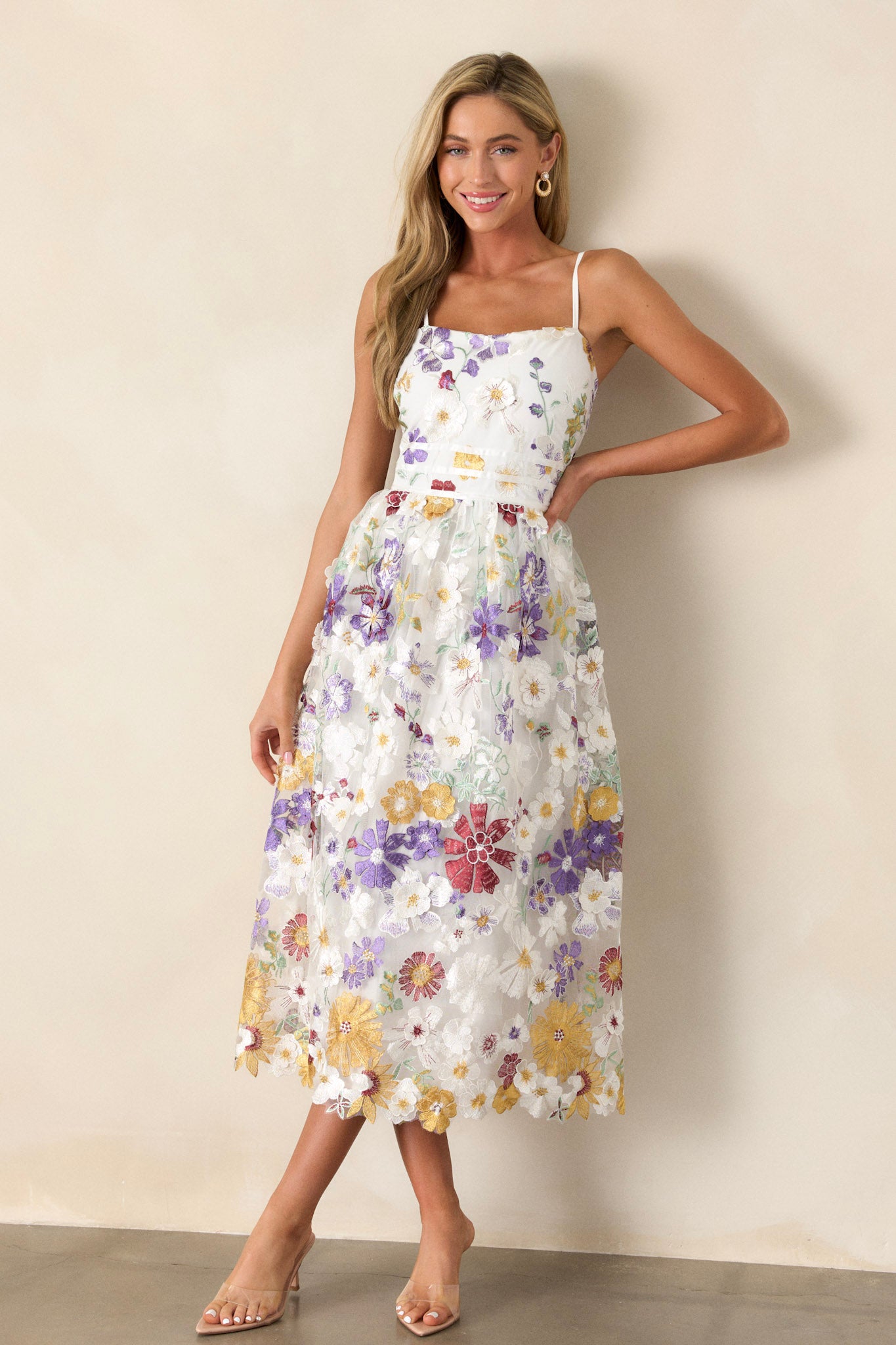 Front angled view of this ivory floral dress featuring a square neckline, multicolor floral embroidery, a back zipper, and adjustable spaghetti straps. 