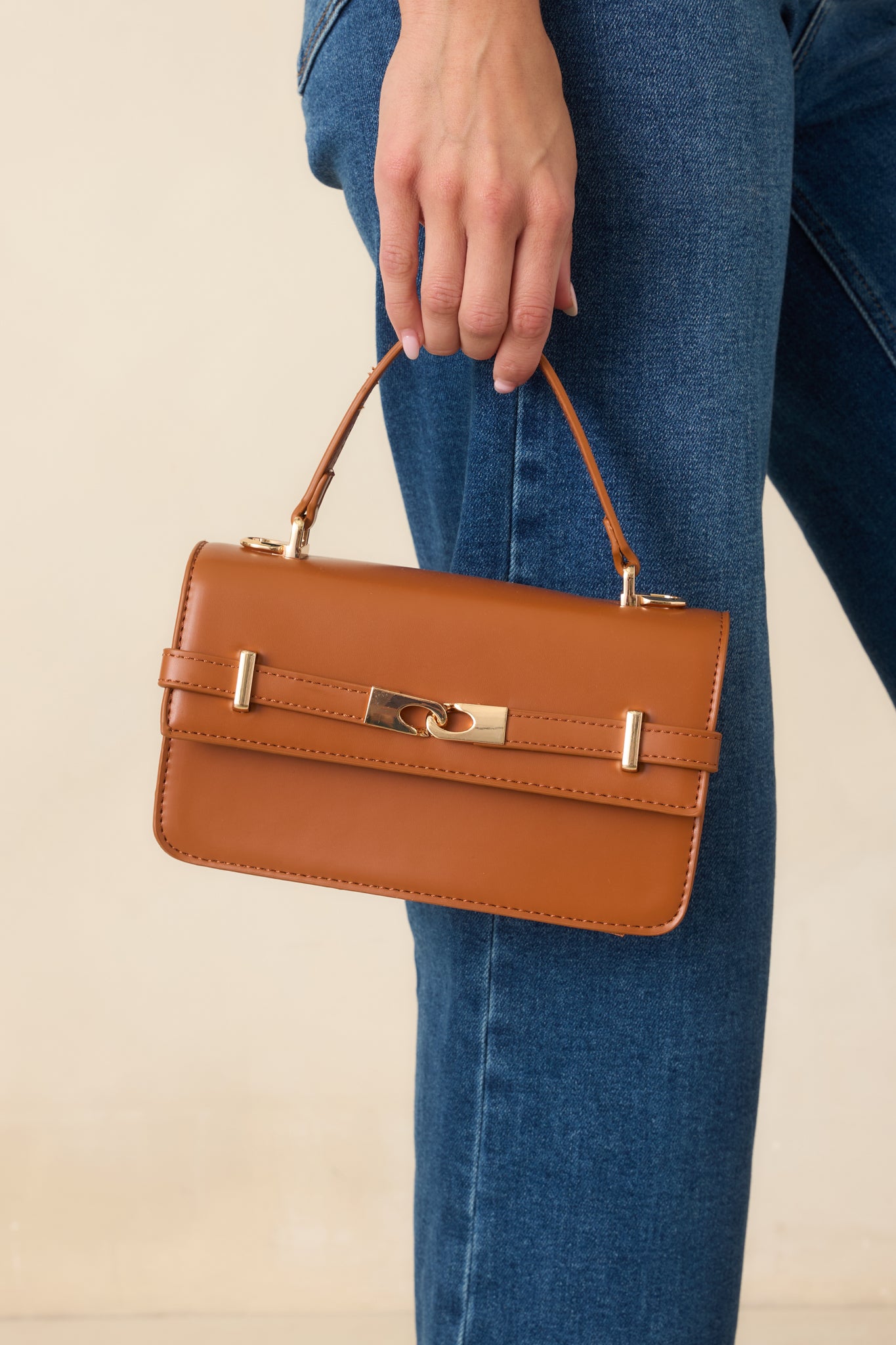 Close view of the handbag highlighting the sophisticated front belt detail, polished gold-tone hardware, and smooth faux leather finish.