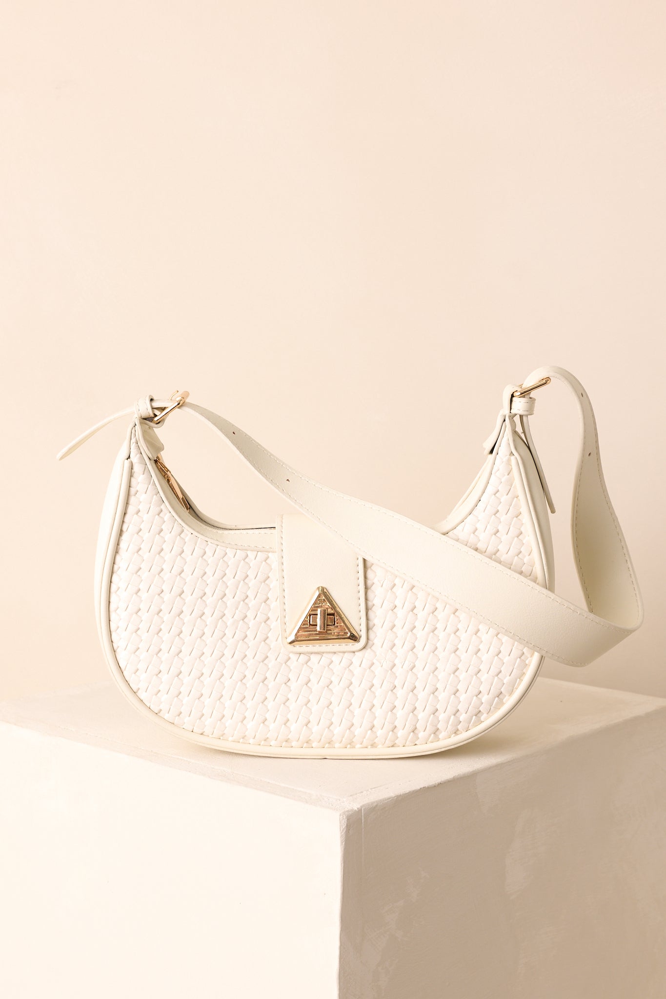 A front view of the white shoulder bag with a half-moon silhouette, woven faux leather design, and gold twist-lock flap closure.