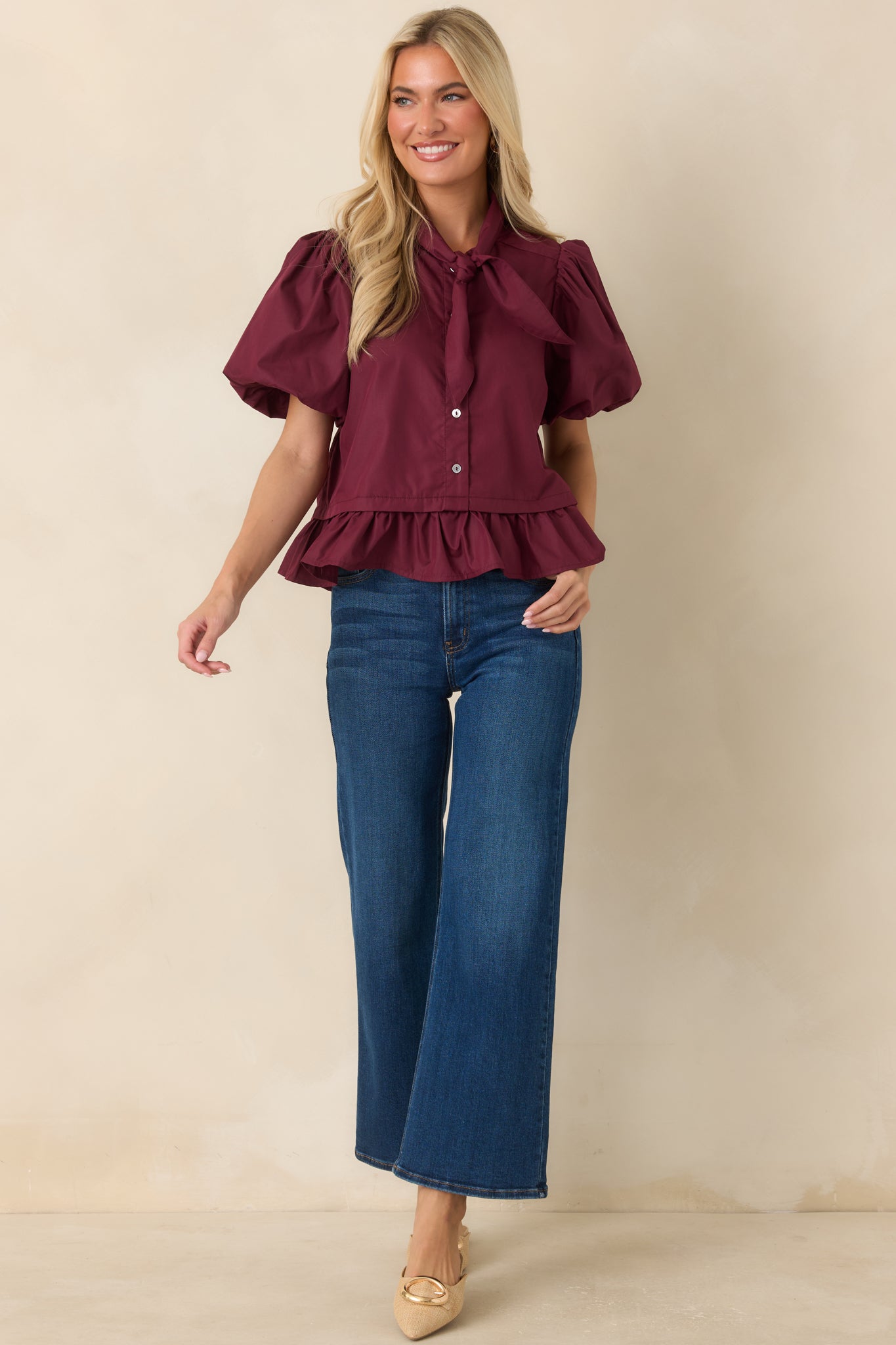 Feminine wine red top showcasing a voluminous sleeve design, tie neckline, and softly flared peplum finish.