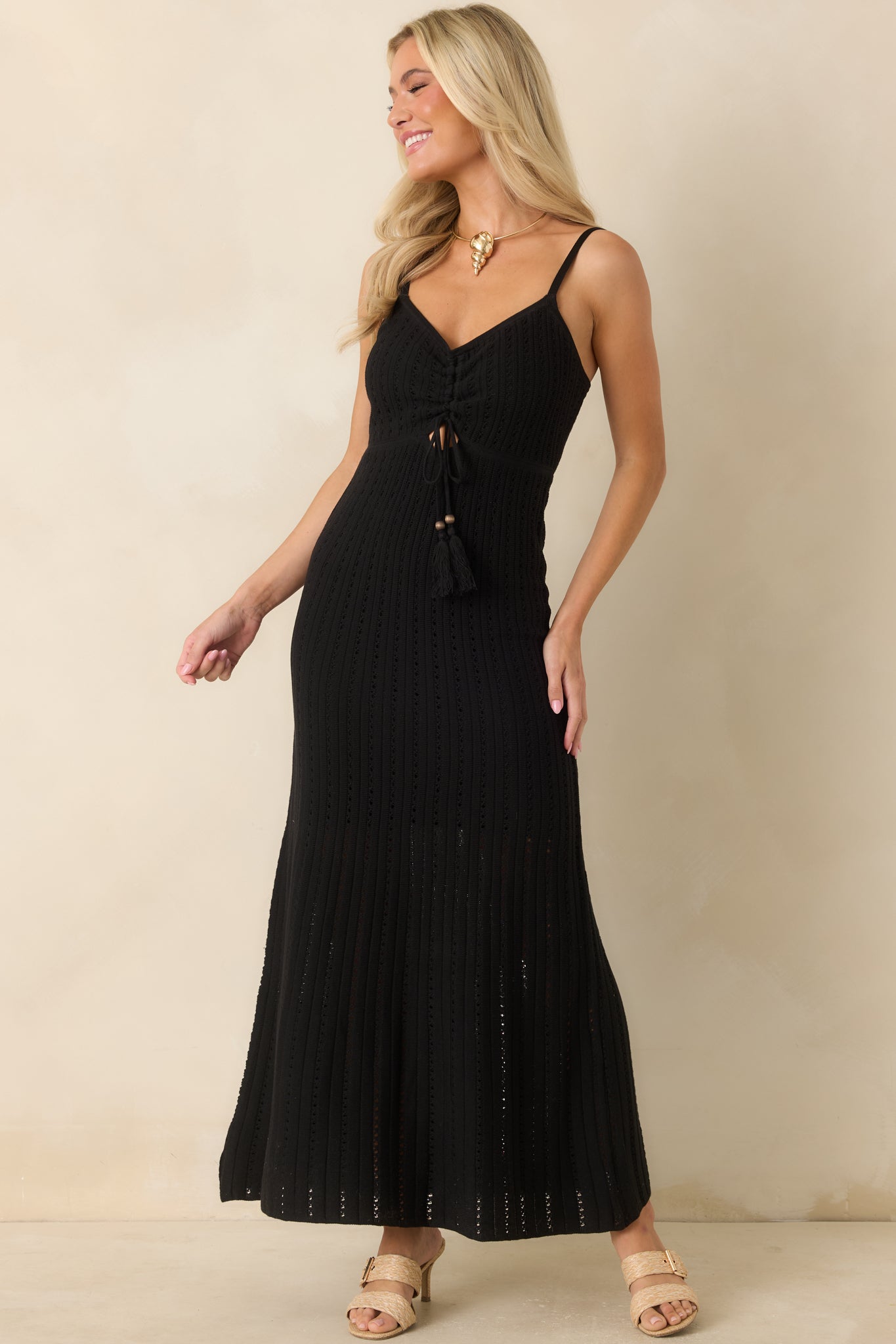 Fitted black crochet maxi dress featuring adjustable straps, an open-knit texture, and a feminine ruched bodice.