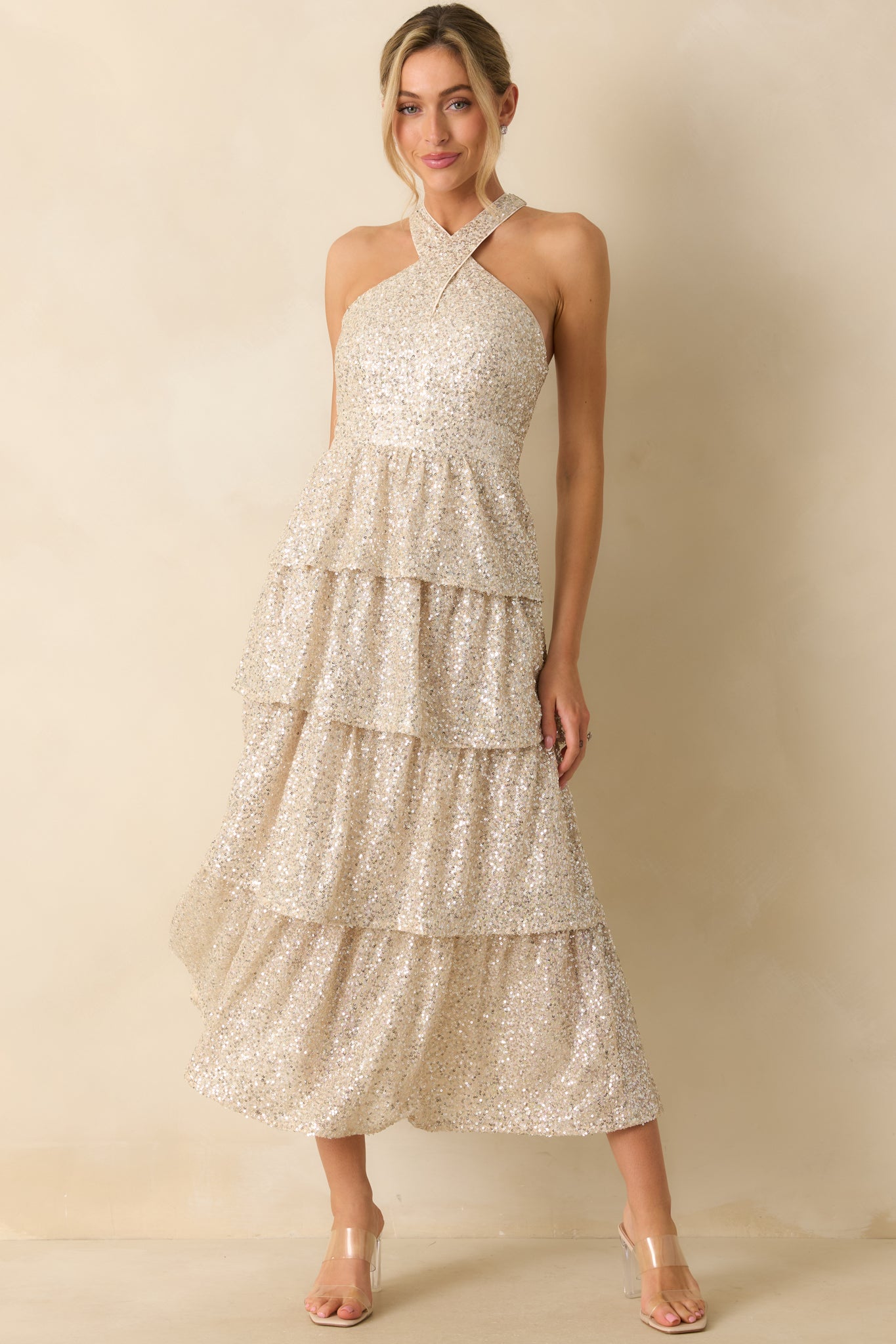 Fitted champagne sequin maxi dress with a structured halter neckline and tiered flowing layers.