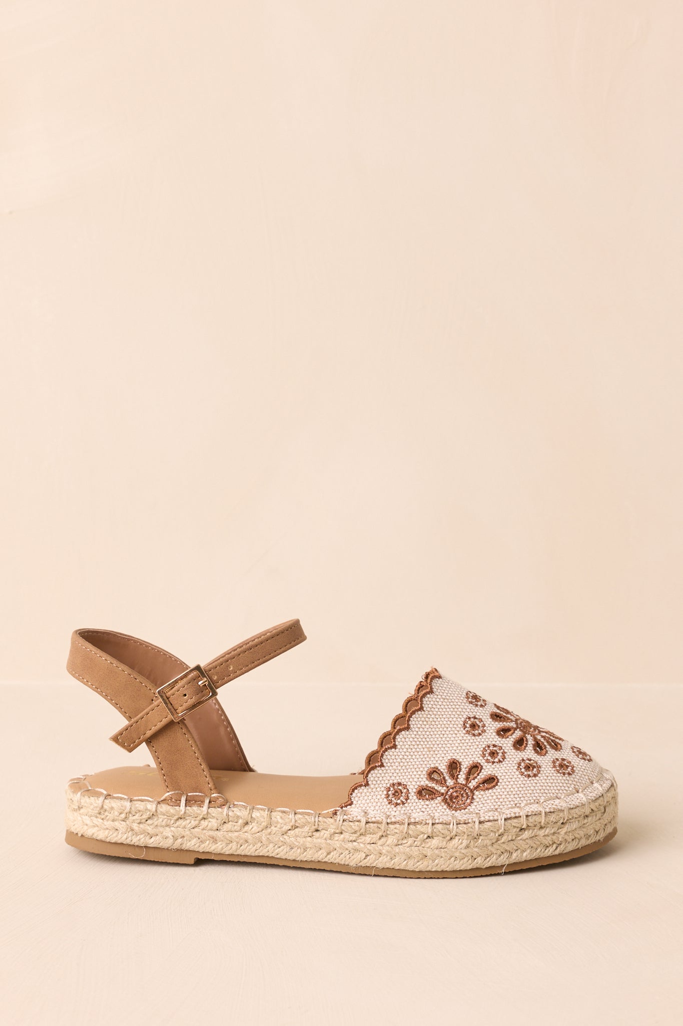 Side view of flat sandal highlighting rounded toe, woven jute sole, and scalloped hem.
