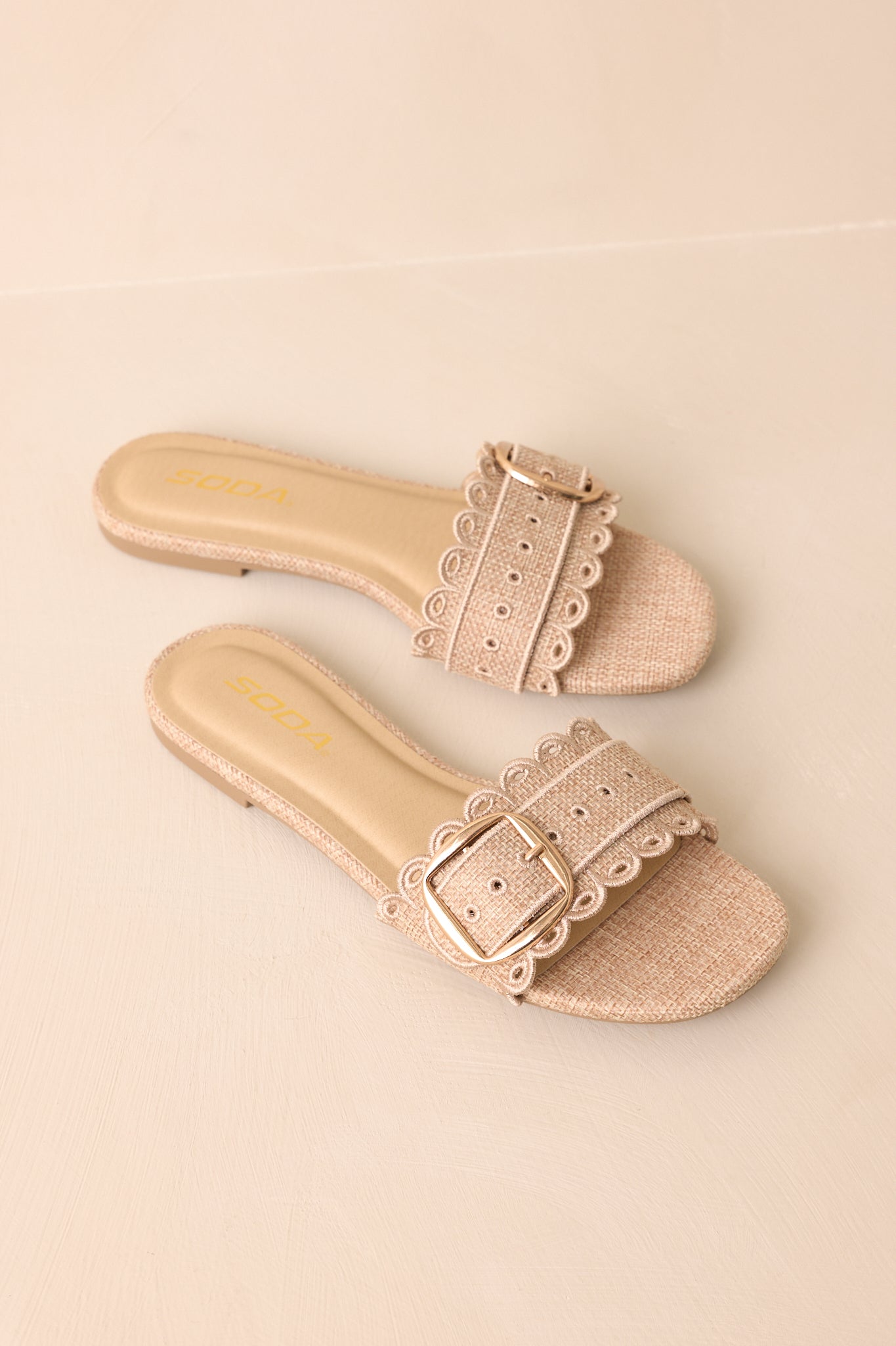Flat sandals with embroidered detailing and gold buckle photographed straight on against neutral background.