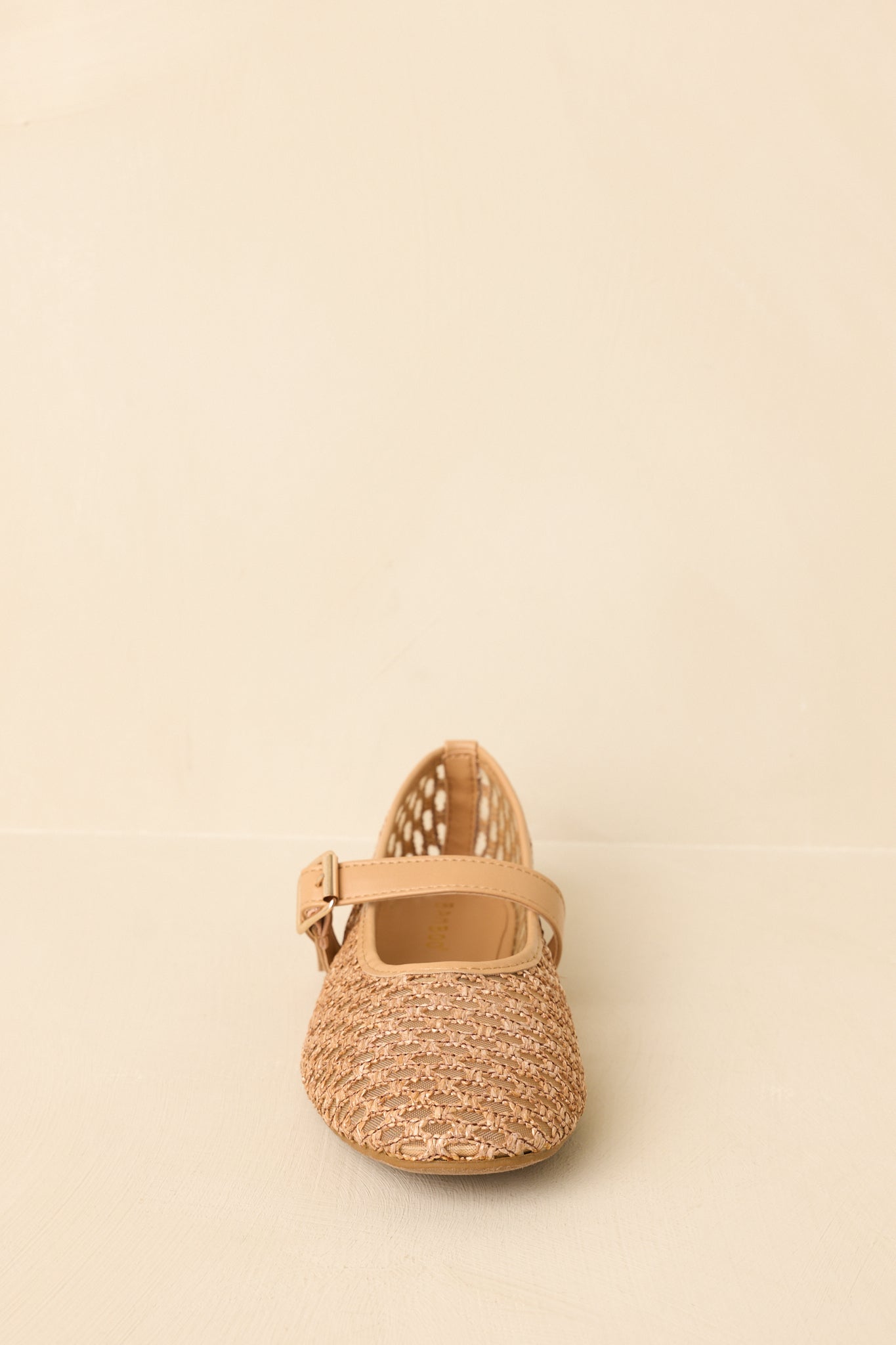 Flats displayed against a beige background with a straight-on view of the rounded toe and strap placement.