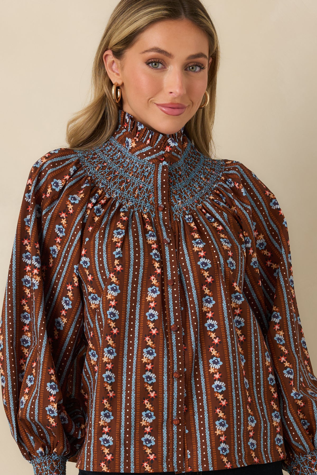 Floral blouse highlighting the voluminous long balloon sleeve and wide blue smocked cuff against the brown background.