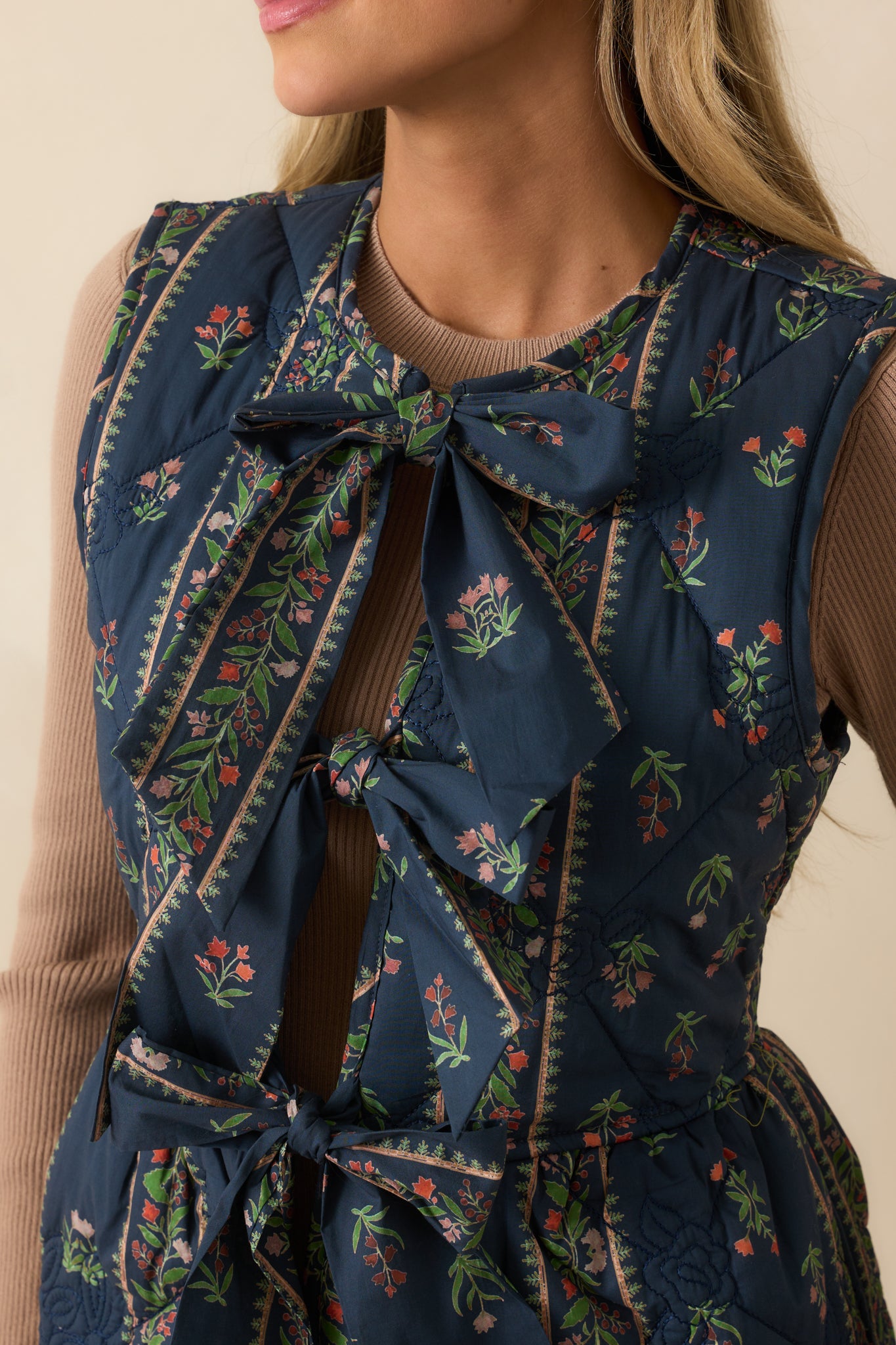 Detailed shot of floral embroidery and bow closure on navy quilted vest.