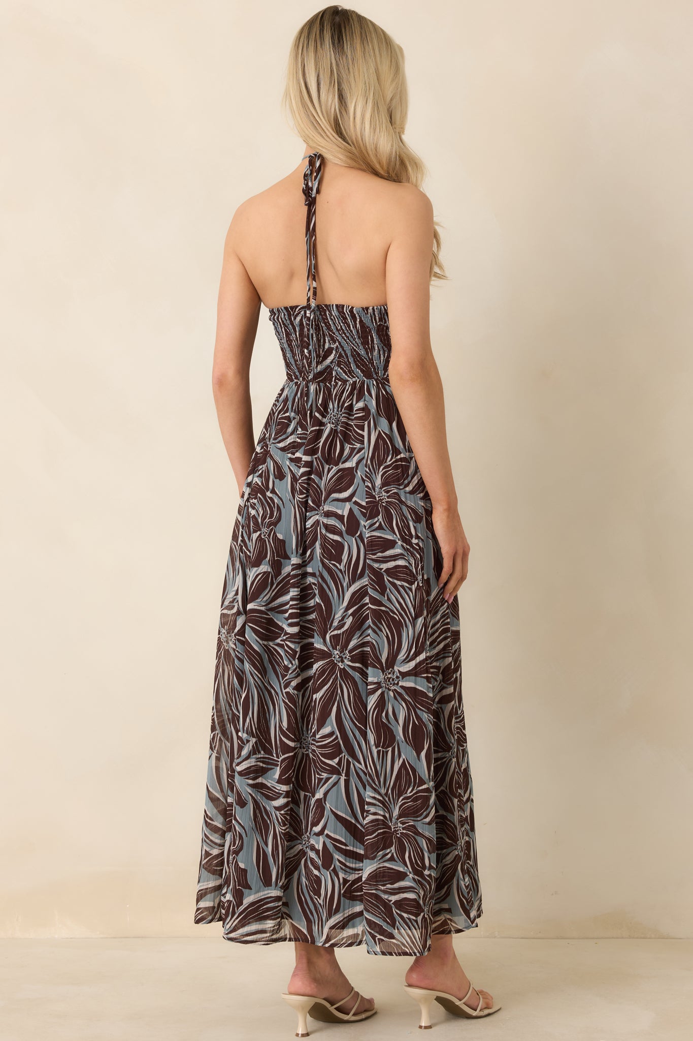 Back view of floral halter maxi dress featuring smocked panel and flowing full-length skirt.