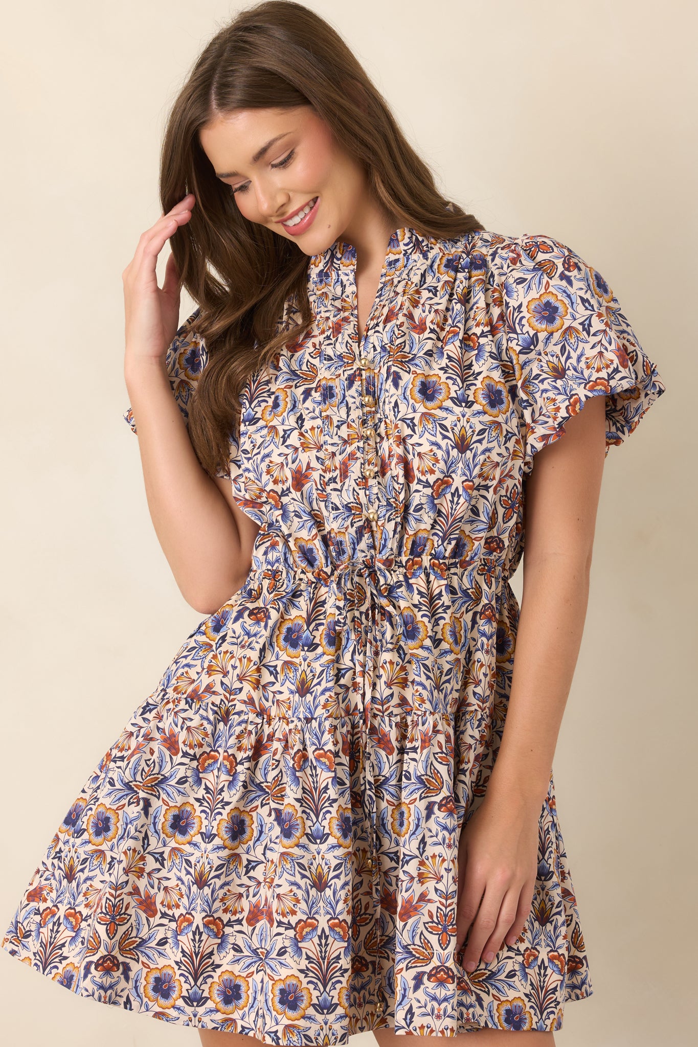 Close view of the mini dress highlighting its split neckline, pleated front, and polished gold-tone buttons.