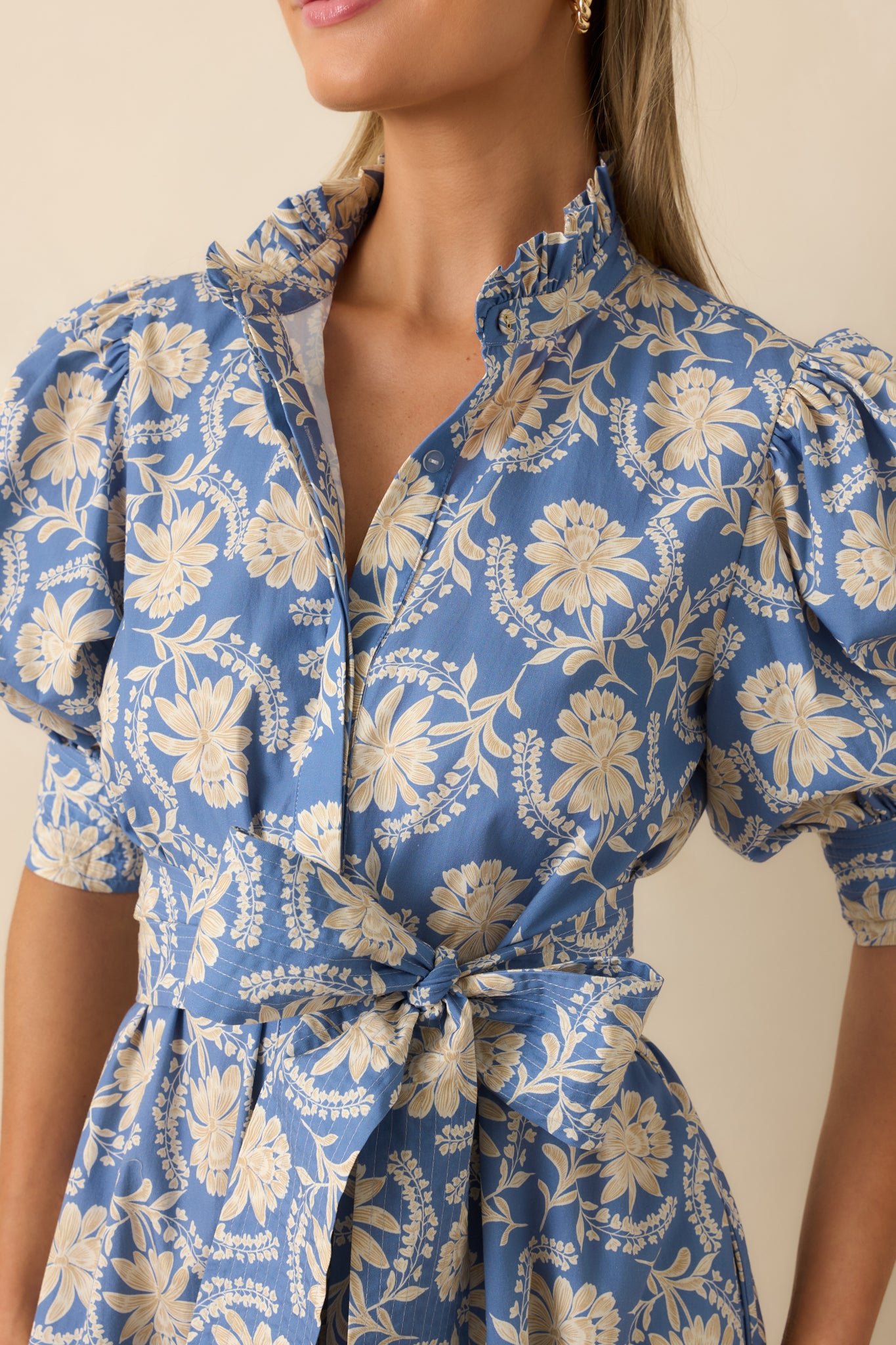 Close-up of the floral cotton dress highlighting the ruffled stand collar, split neckline, smocked cuffs, and dusty blue floral print.