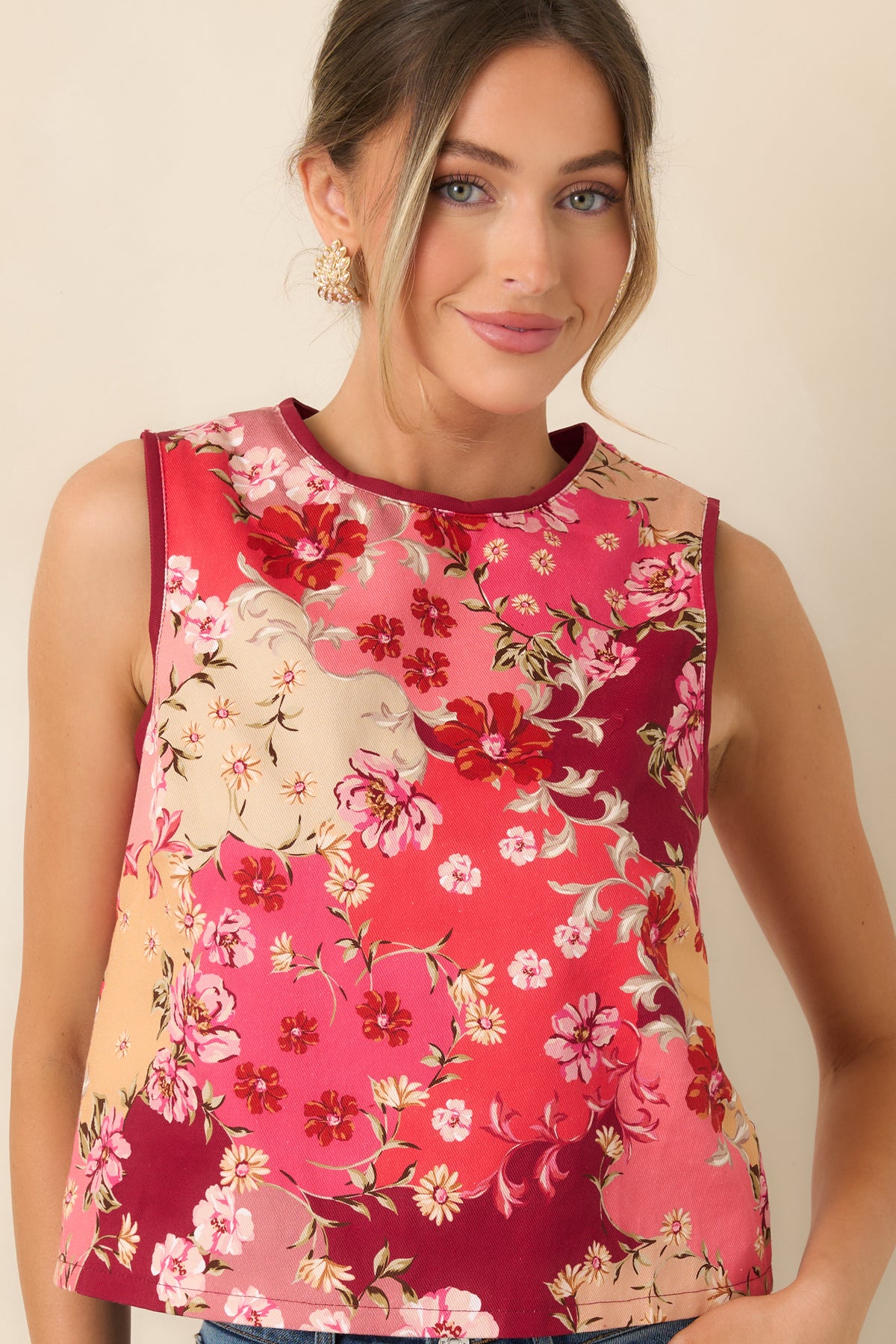 Burgundy trim defines the armholes of the relaxed floral top, framing pink and cream blossoms with green foliage.