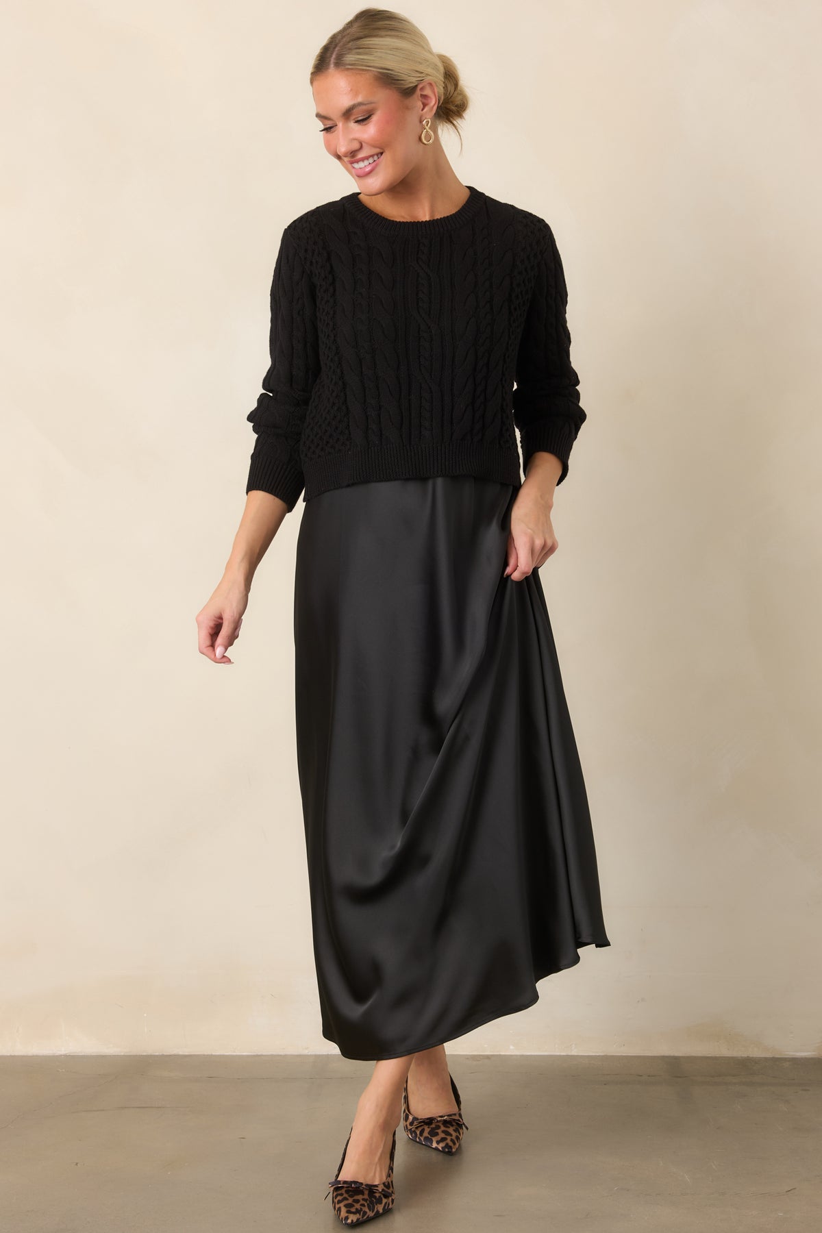 Fluid satin maxi dress styled with a cropped cable-knit sweater, creating a softly layered A-line silhouette.