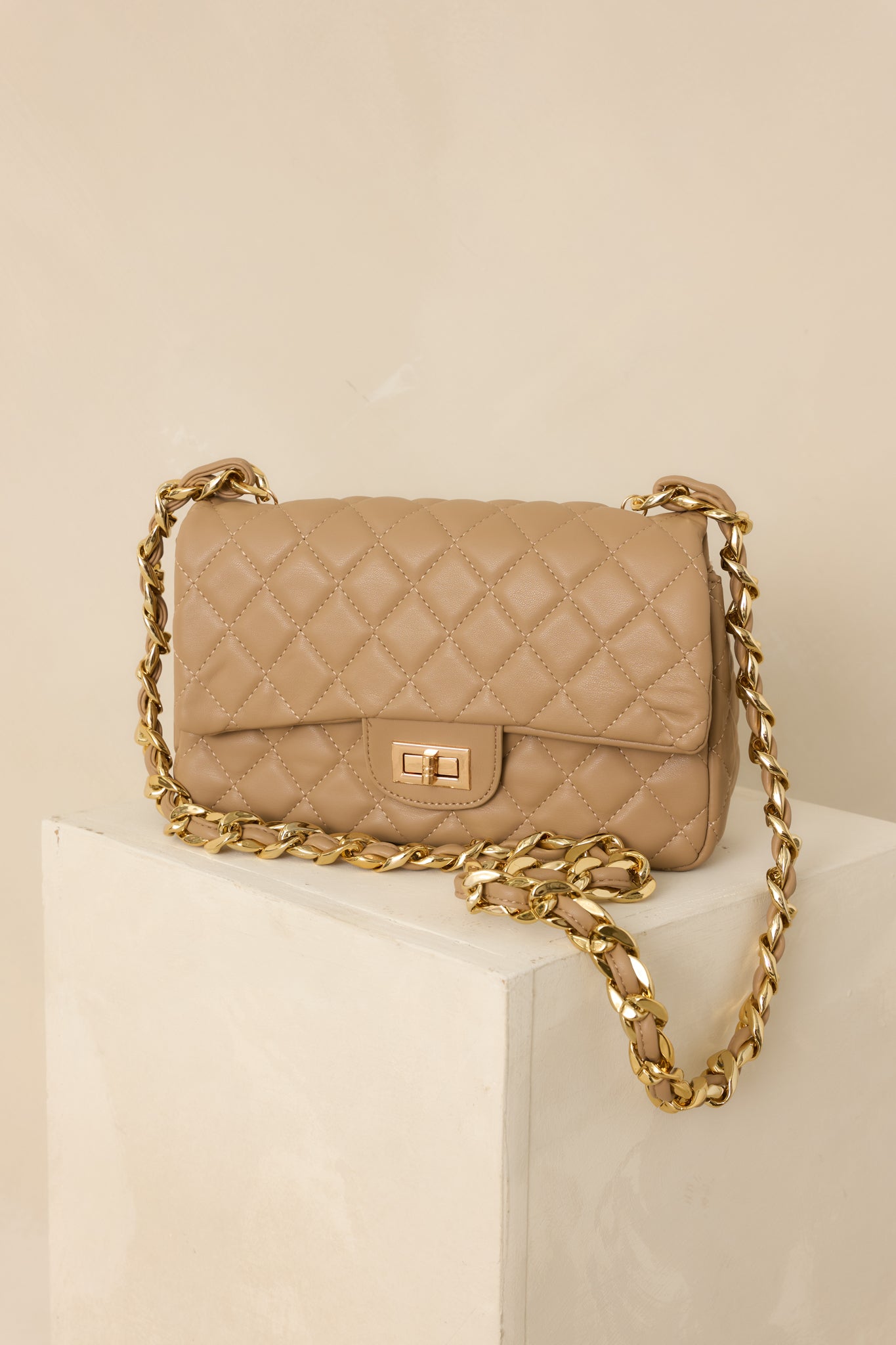 Cropped view focusing on the quilted taupe faux leather and gold twist lock closure.