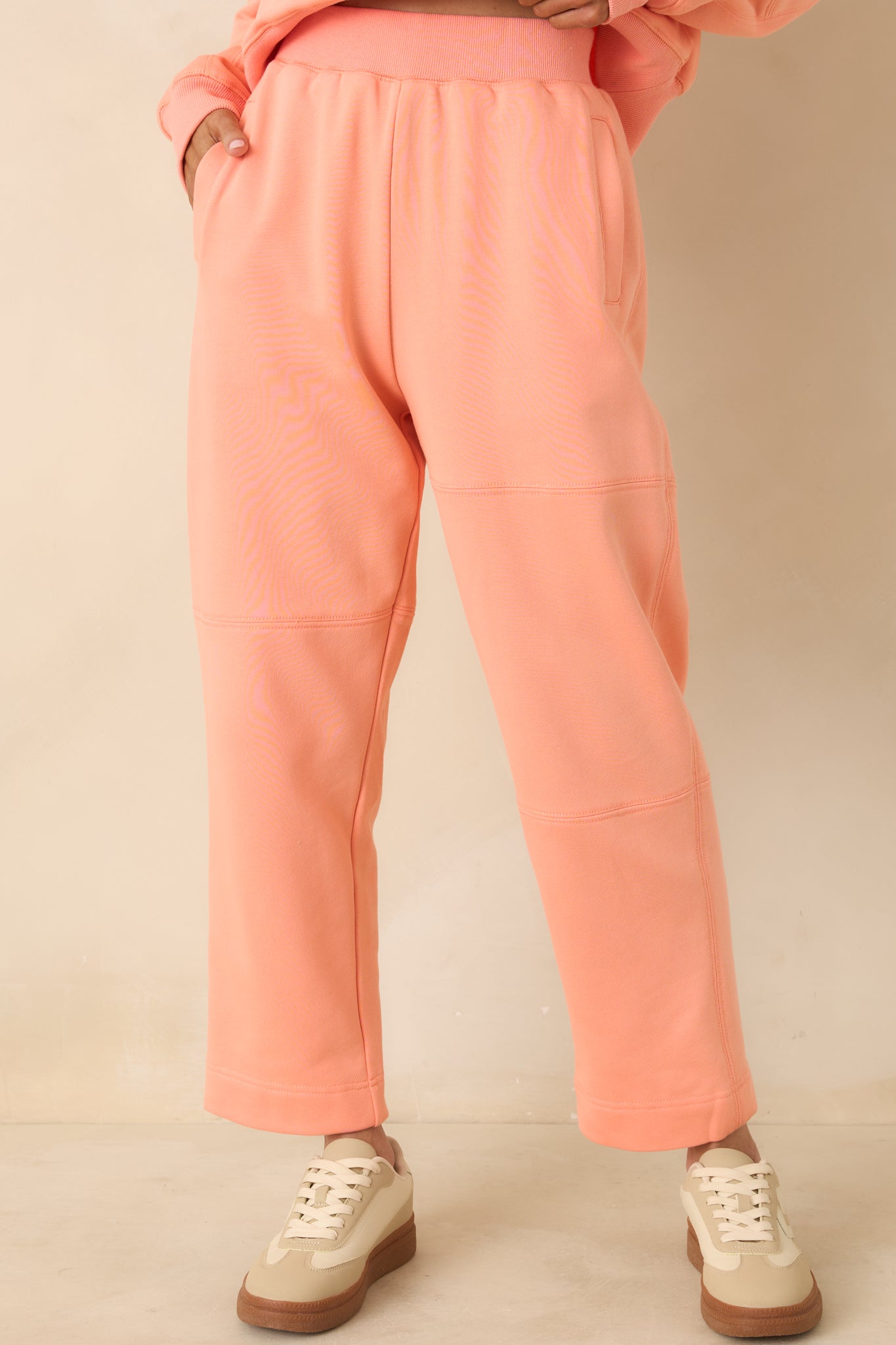 Focused view of block-stitched seam details and tapered ankle on coral sweatpants.