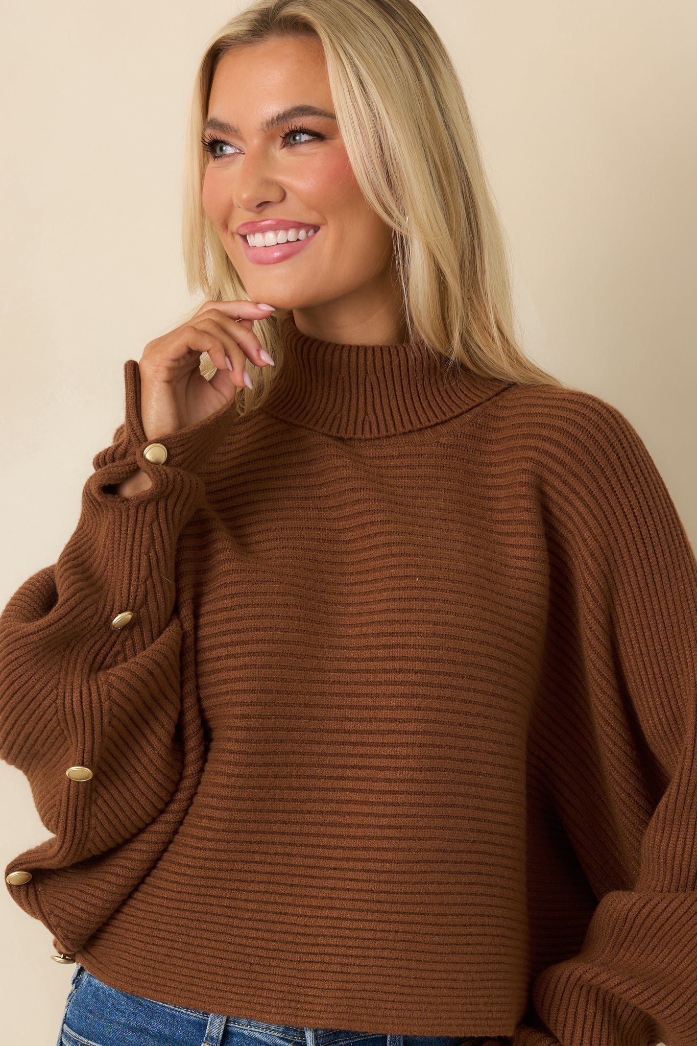 Focused view of draped brown batwing sleeves and pullover silhouette.