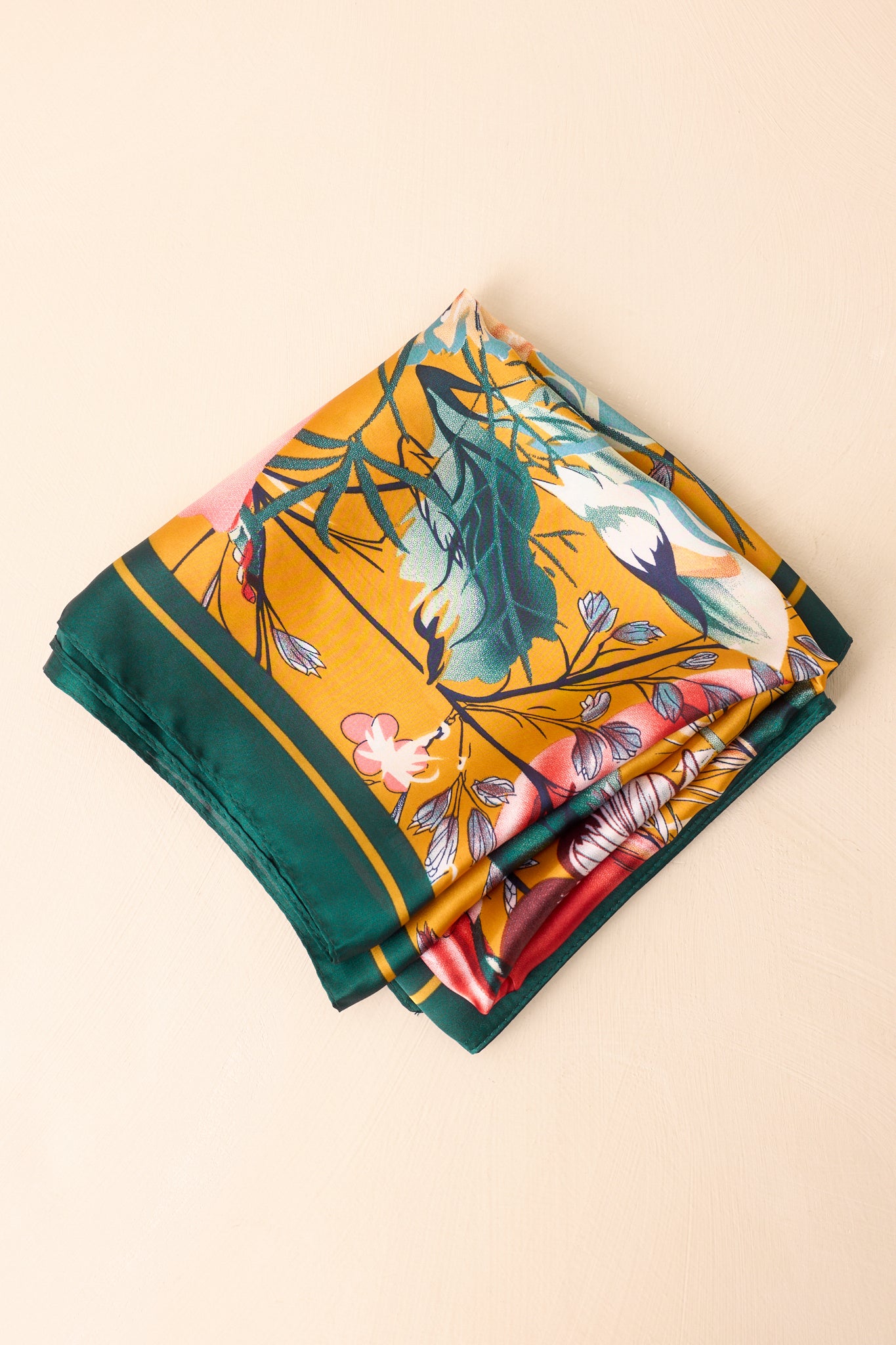 A view of the hair scarf folded, highlighting its green border, gold background, and flower field print.