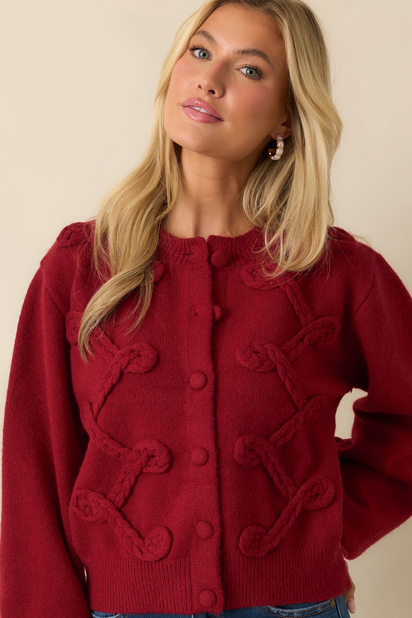 Front-focused crop showing long sleeves and textured braided appliqué on the red knit cardigan.