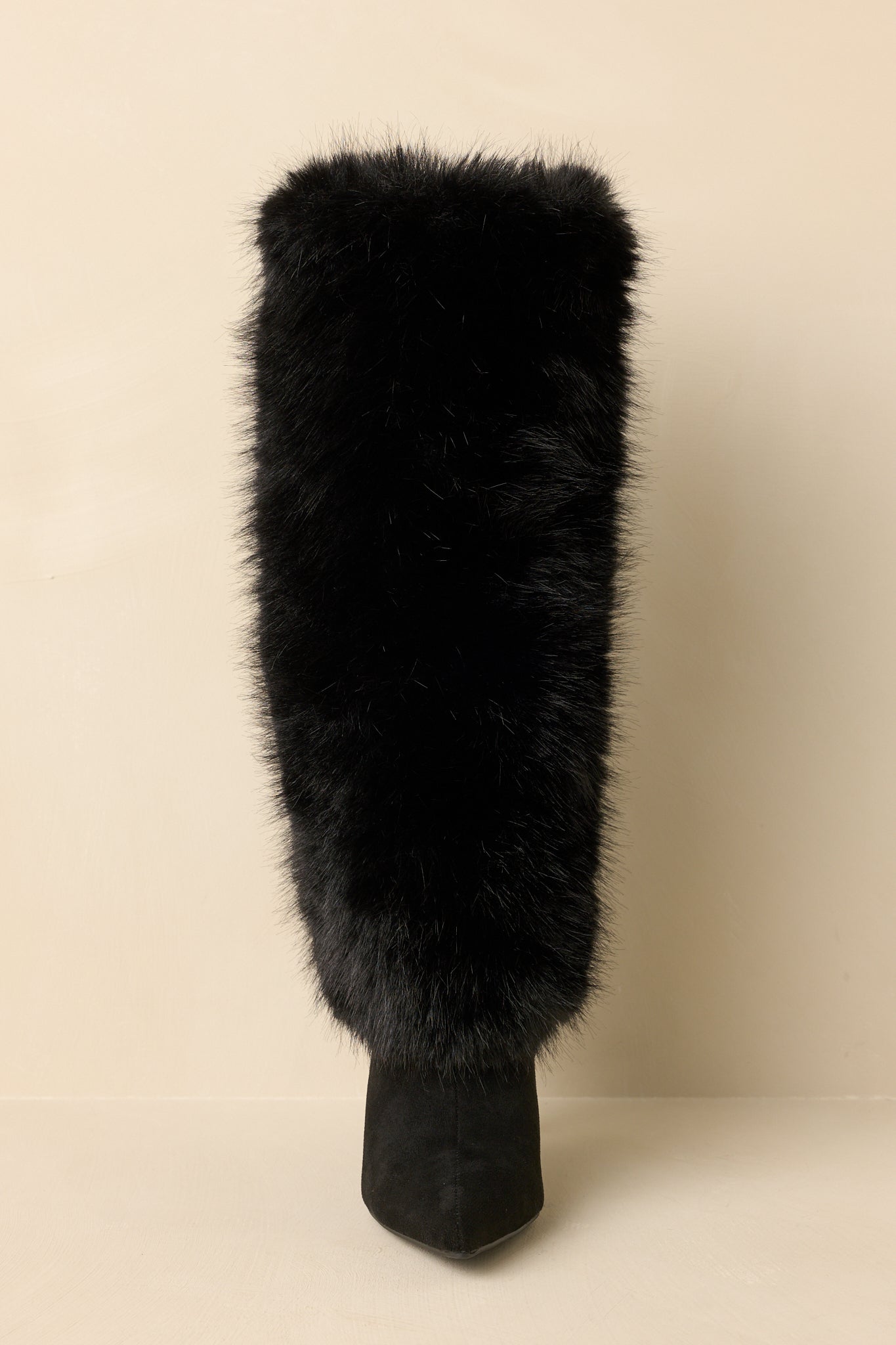 Front-facing view of black knee-high stiletto boots against a beige background highlighting the pointed toe and slim high heel.