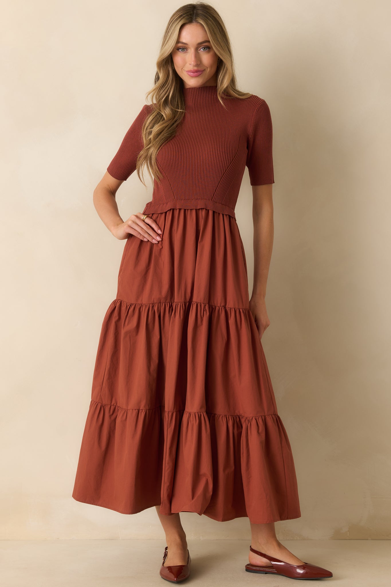 Front-facing rust red maxi dress with a structured bodice, short sleeves, and tiered skirt movement.