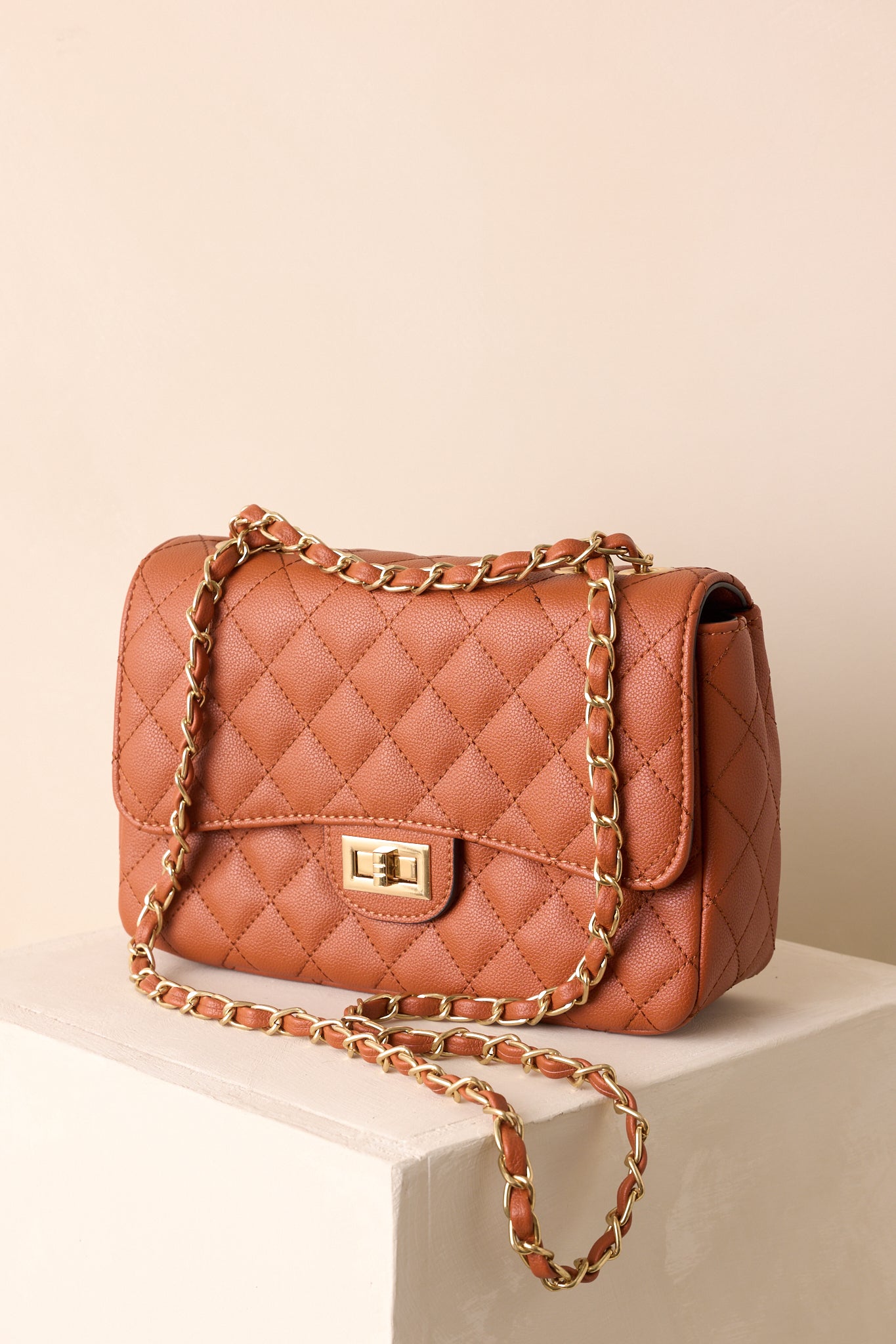 Front flap twist-lock closure on the ginger brown handbag with sleek quilted texture.