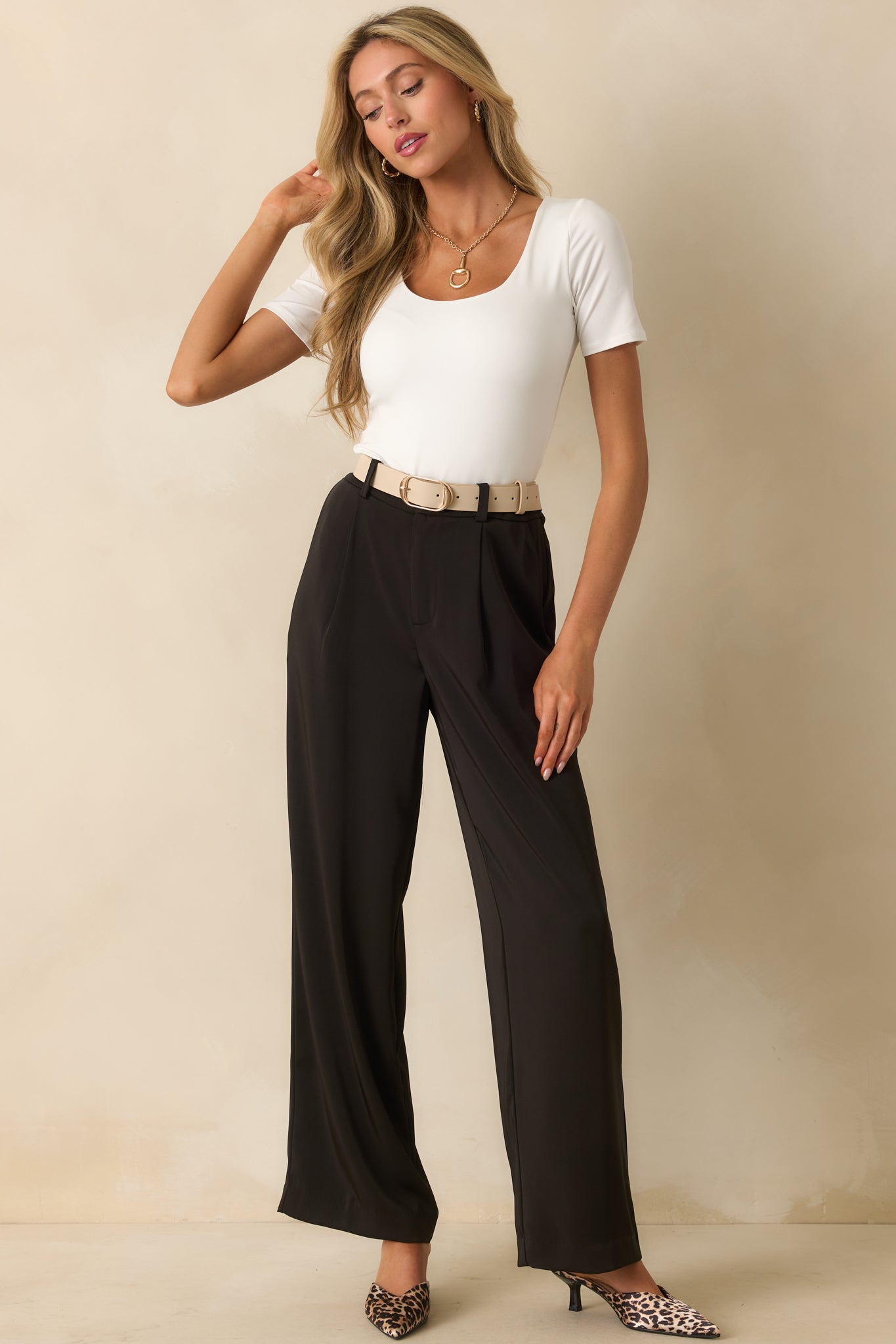 Front view of black trousers with pleated hips and a relaxed yet tailored wide-leg cut.