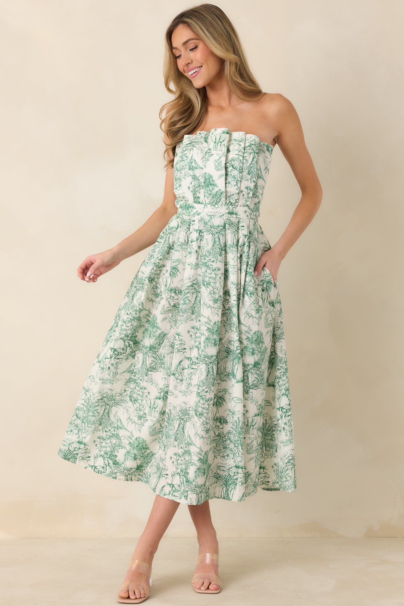 Front view of strapless green toile midi dress featuring a pleated bodice, slightly pleated skirt, and functional hip pockets.