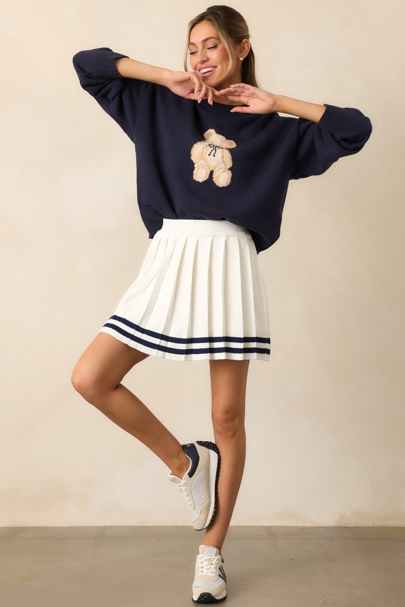 Front view of the ivory pleated skirt showcasing an elastic waistband, airy knit fabric, and navy stripes along the hem for a classic contrast.
