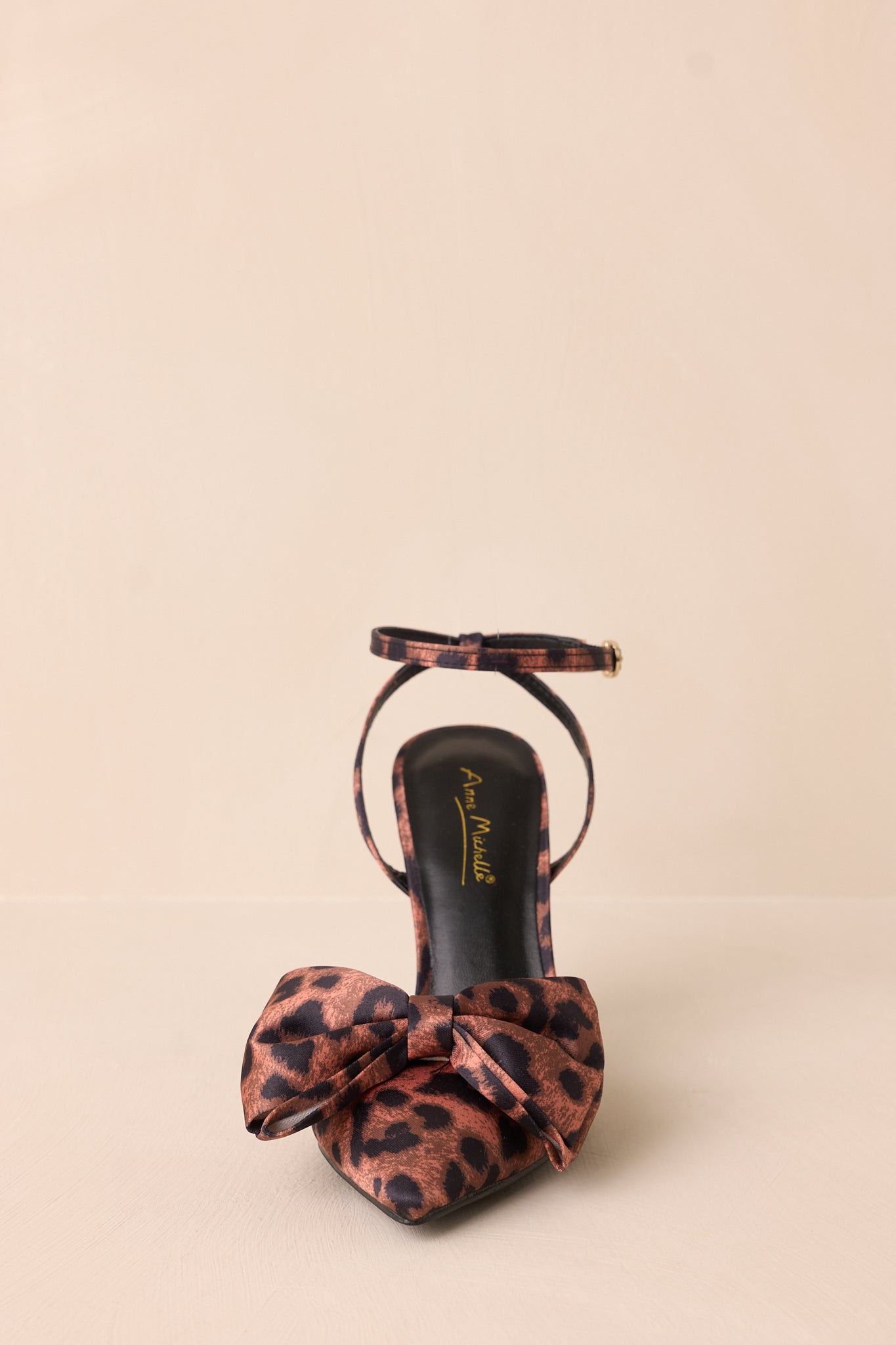 Front view of the leopard print heels against a beige background showcasing the pointed toe and bow accent.