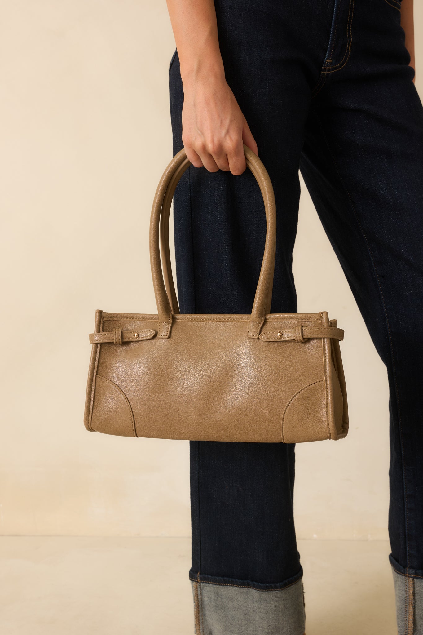 A front view of the light mocha handbag featuring a rectangular silhouette, rolled double top handles, and belted side detailing.
