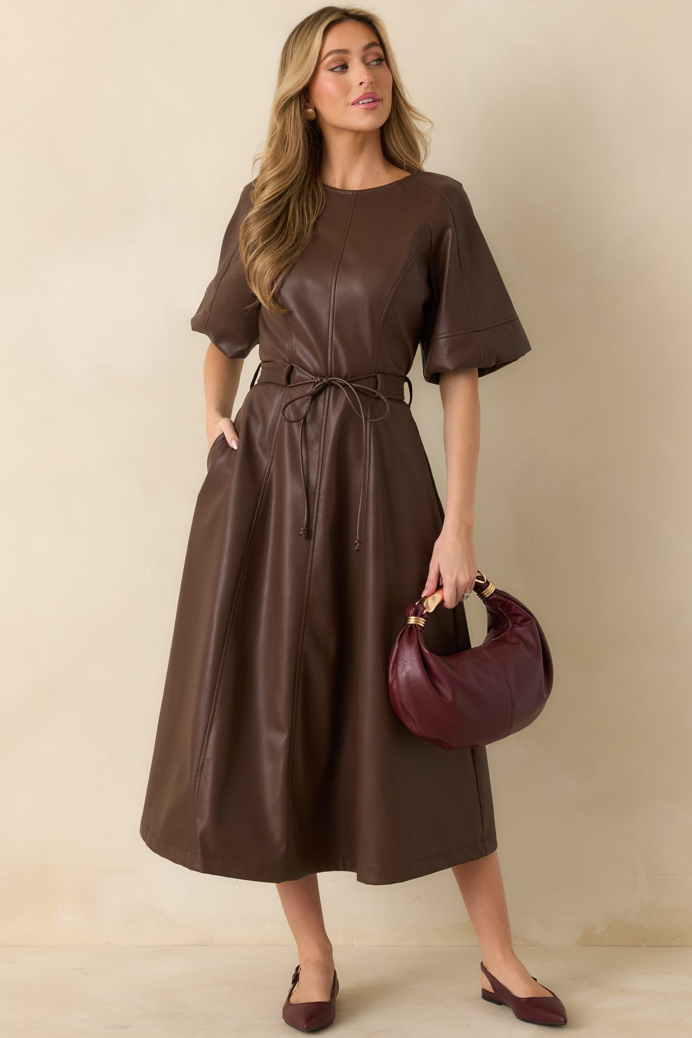 Full front view of brown faux leather midi dress showing short raglan sleeves, crew neckline, and adjustable waist tie.