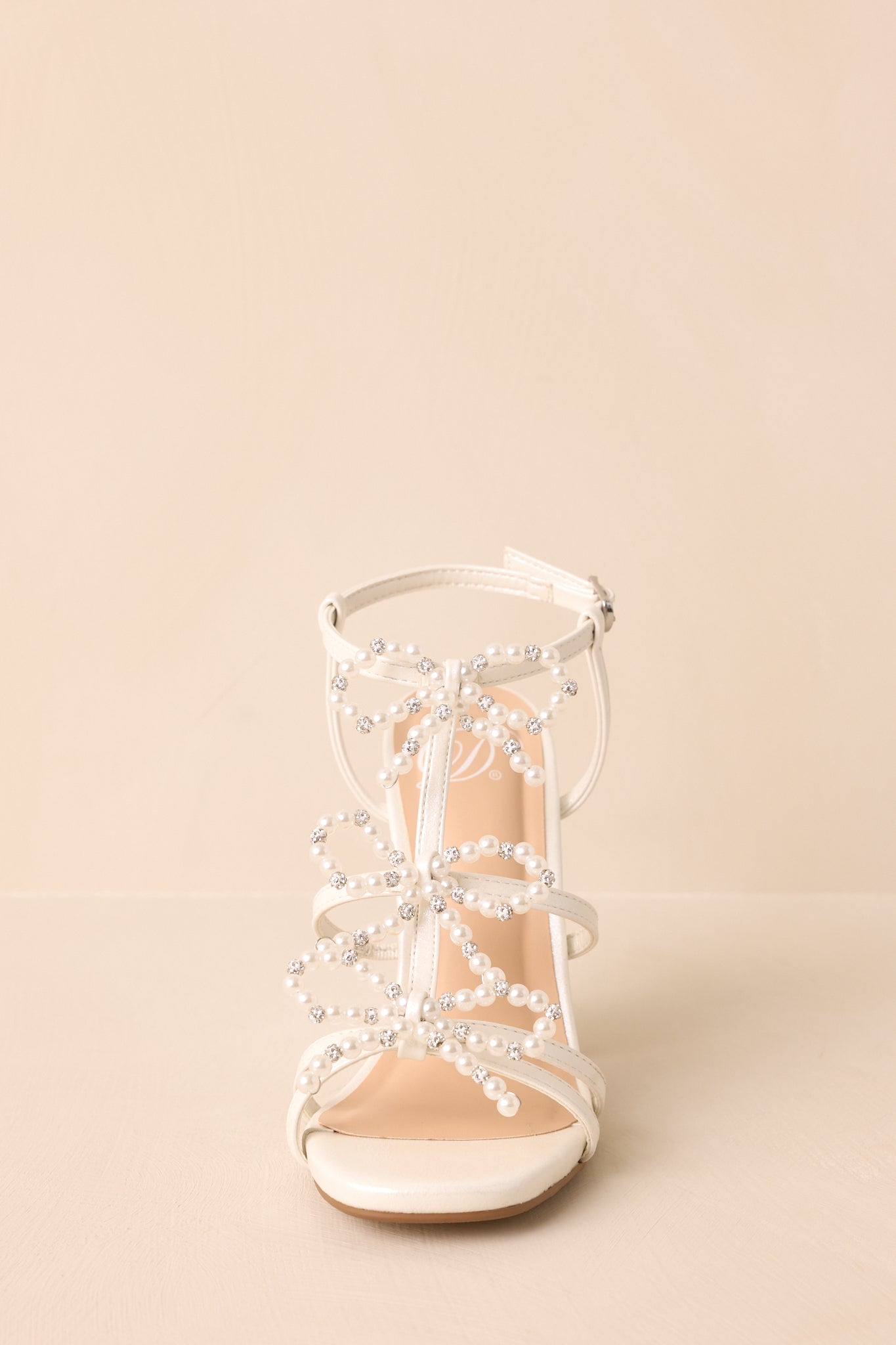 A complete front view of the ivory heels capturing the three decorative bows and their faux pearls and rhinestones.