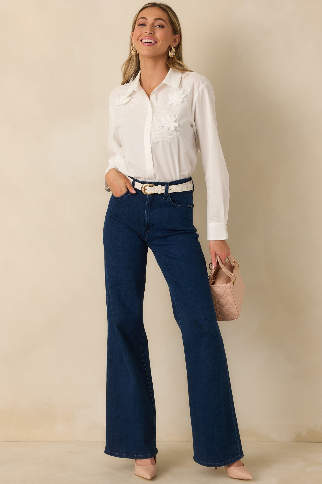 Front view of lightweight white blouse featuring collared neckline and floral appliqué design, styled with sleeves buttoned at the cuffs.